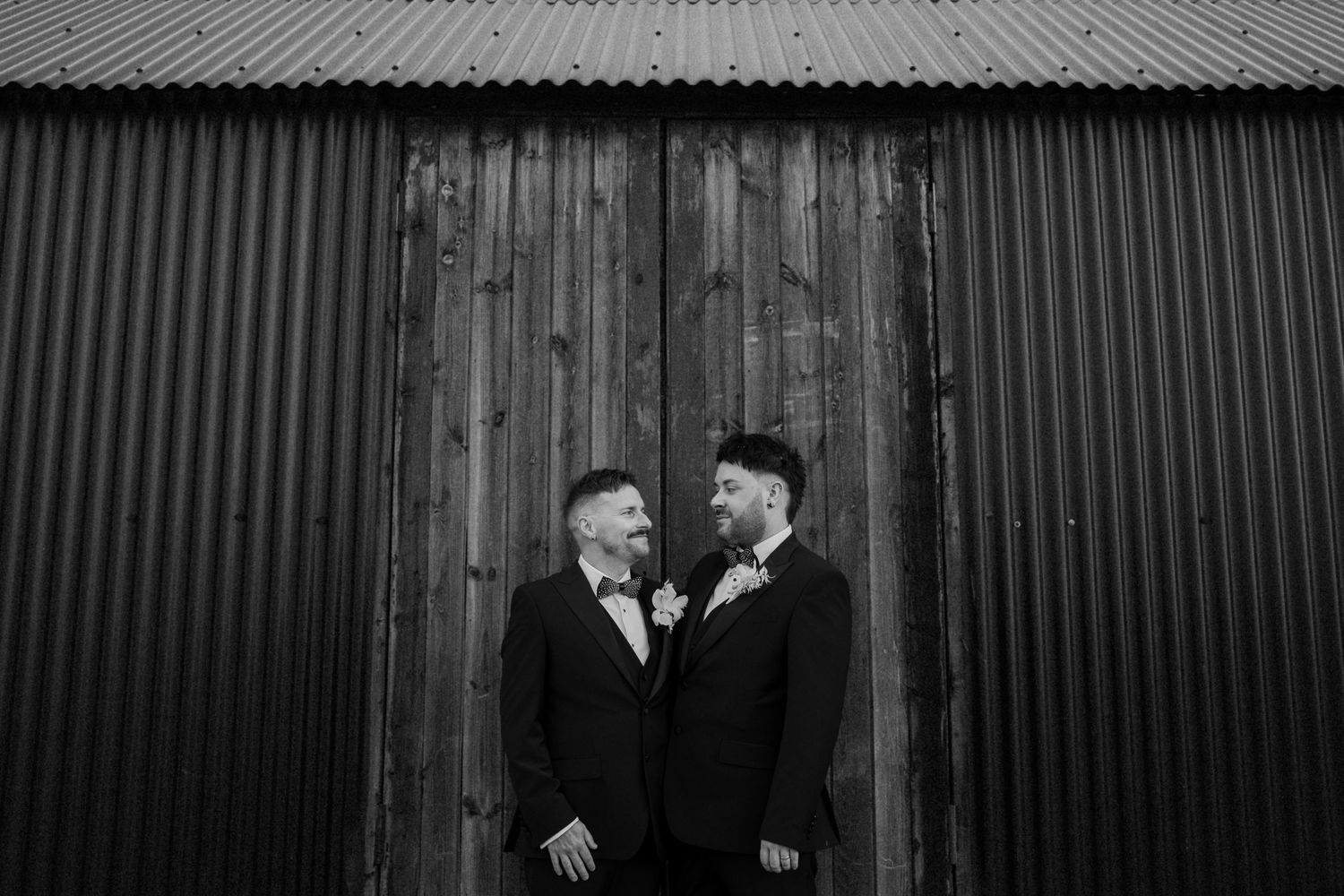 Two people in formal attire standing against rustic corrugated metal wall at The Manor House at Quorn.