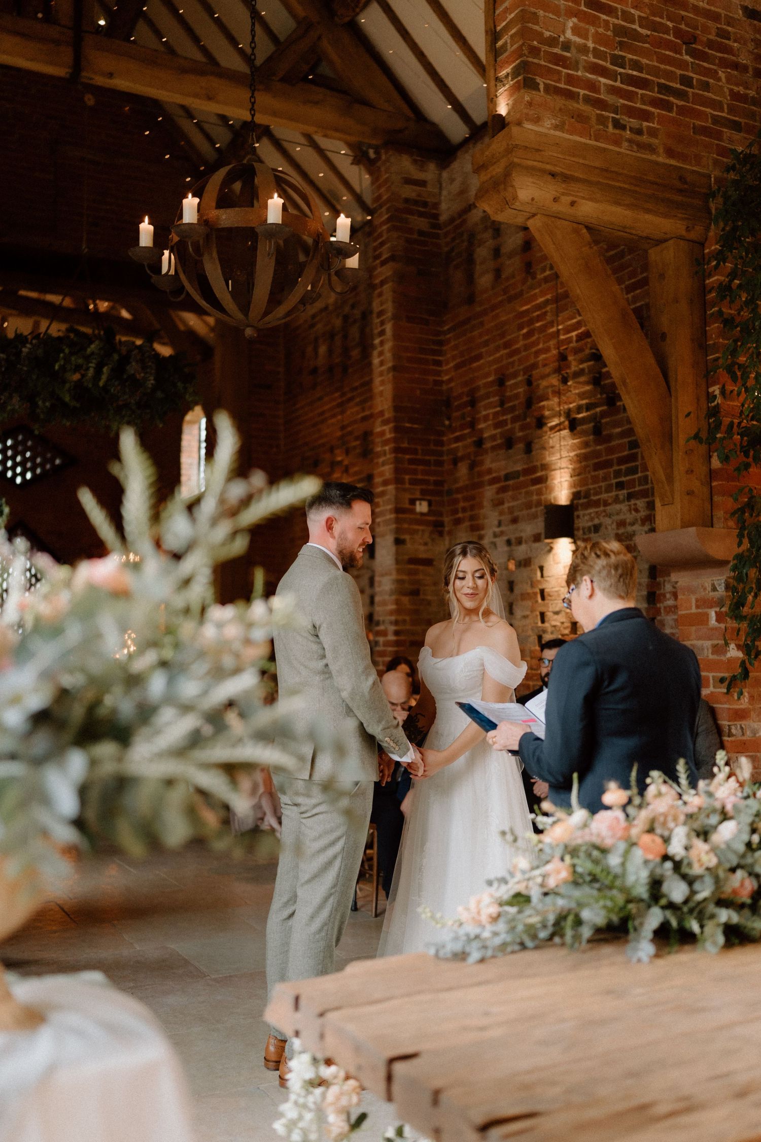 An intimate wedding ceremony in a rustic brick barn with exposed wooden beams and floral decor at Shustoke Barn.