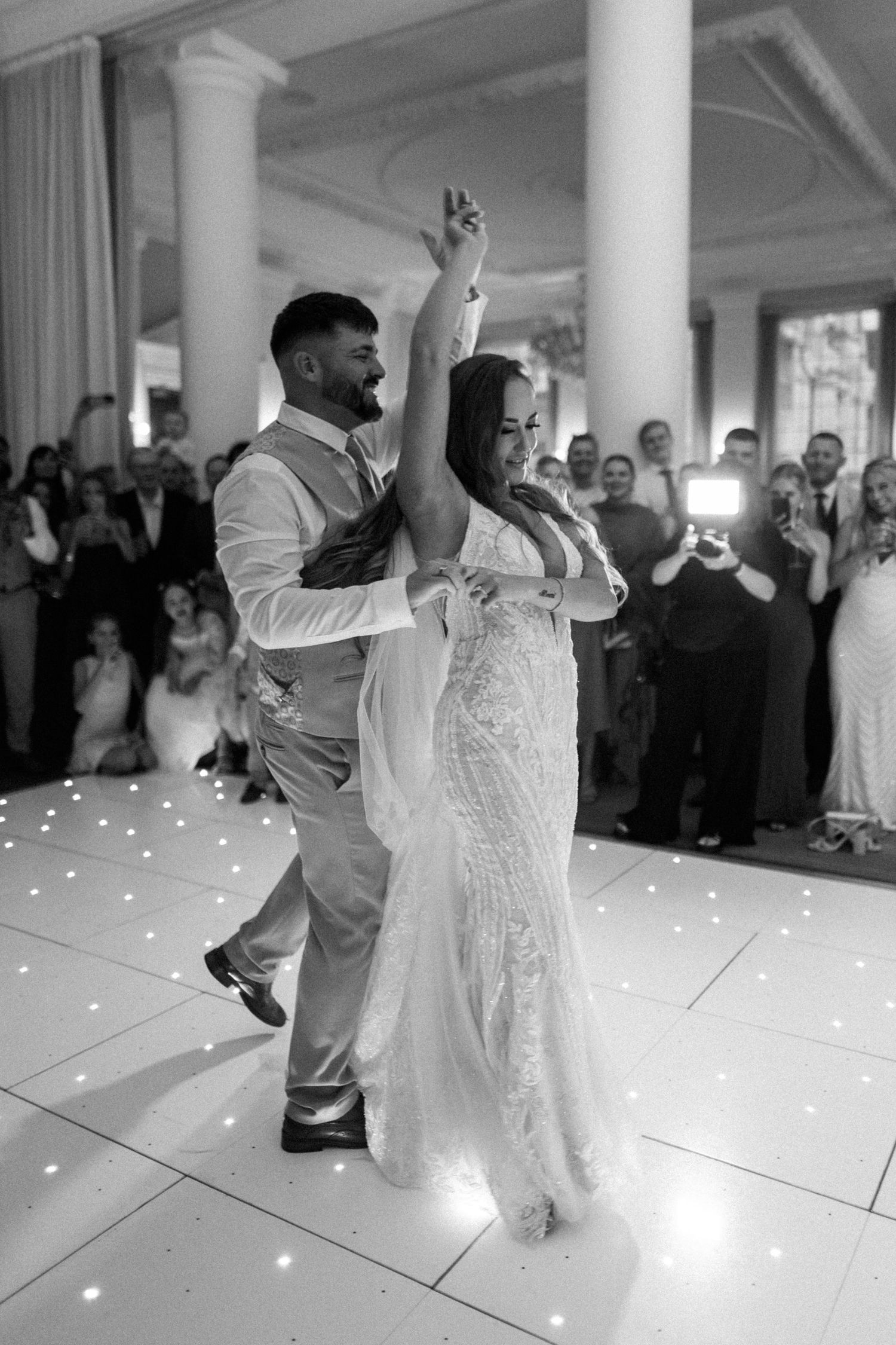 Bride and groom share romantic first dance on illuminated starlight dance floor at elegant white reception venue.