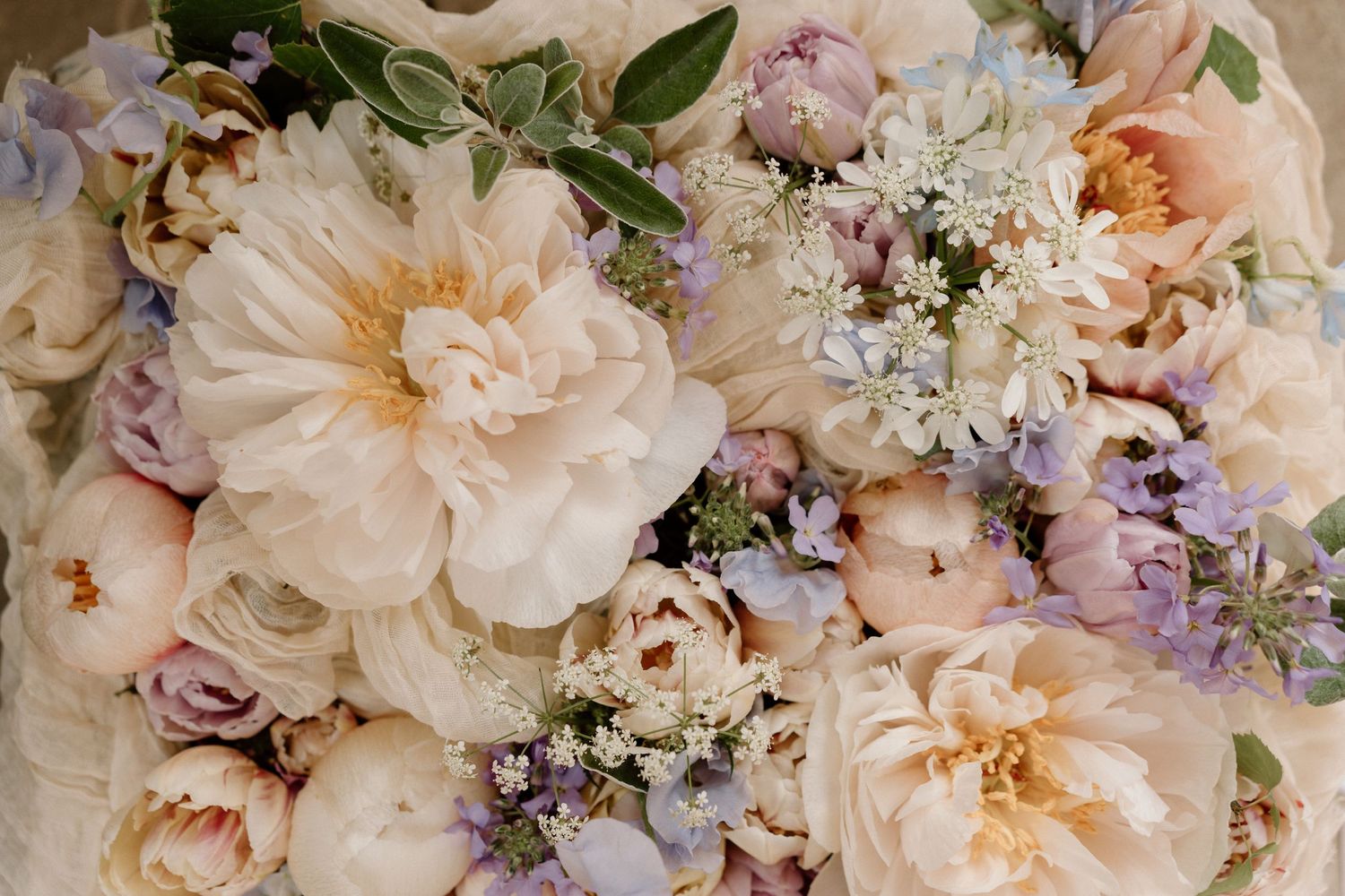 A lush floral arrangement featuring peachy-pink garden roses and delicate purple accents.
