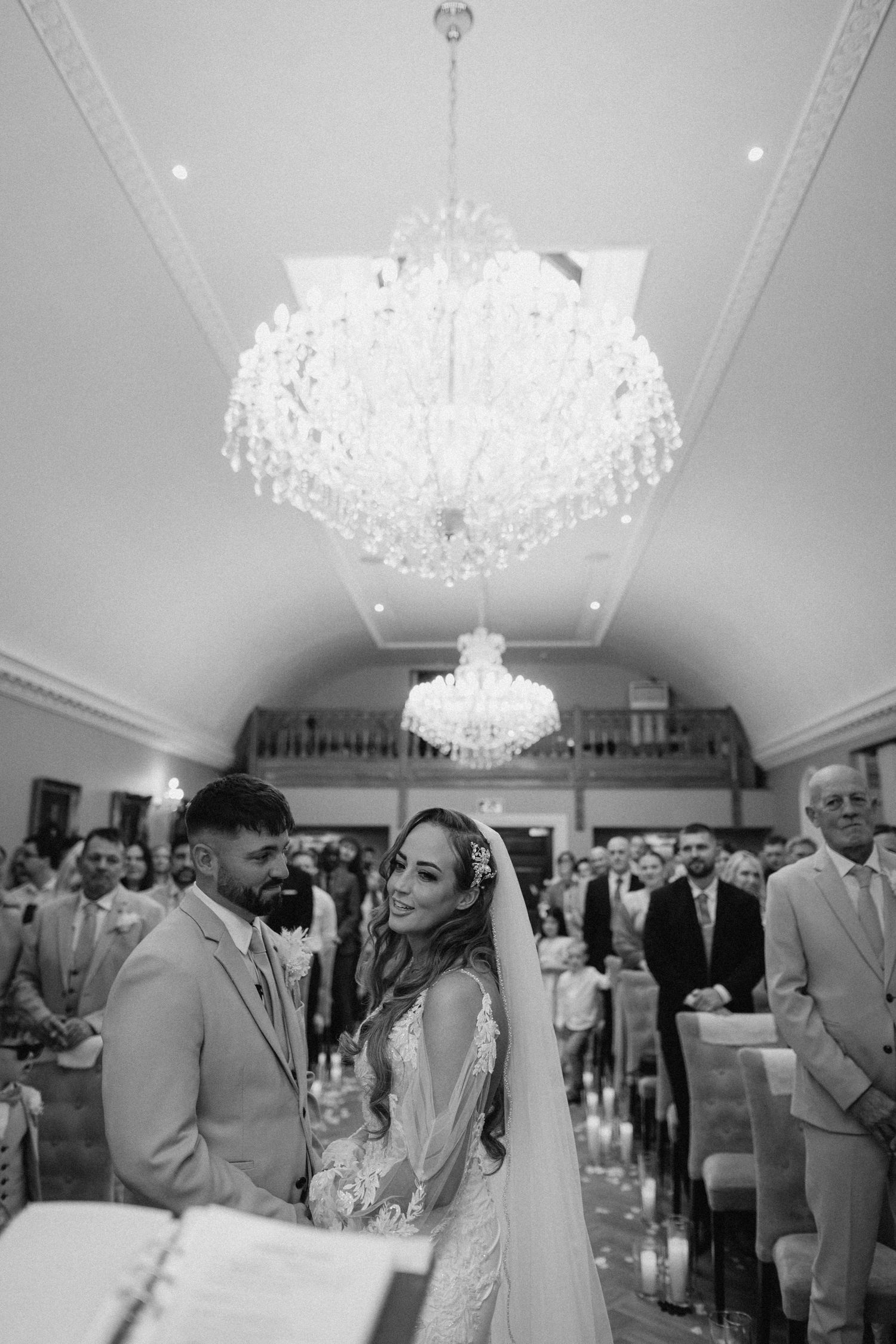 An elegant wedding ceremony in a grand ballroom with crystal chandeliers overhead.
