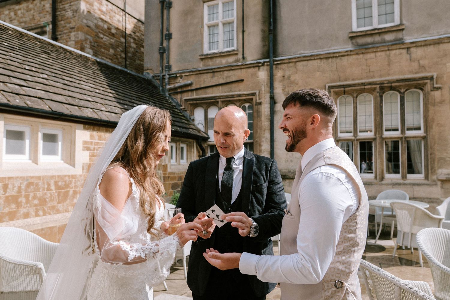 An outdoor wedding ceremony takes place on a stone patio outside a historic building.