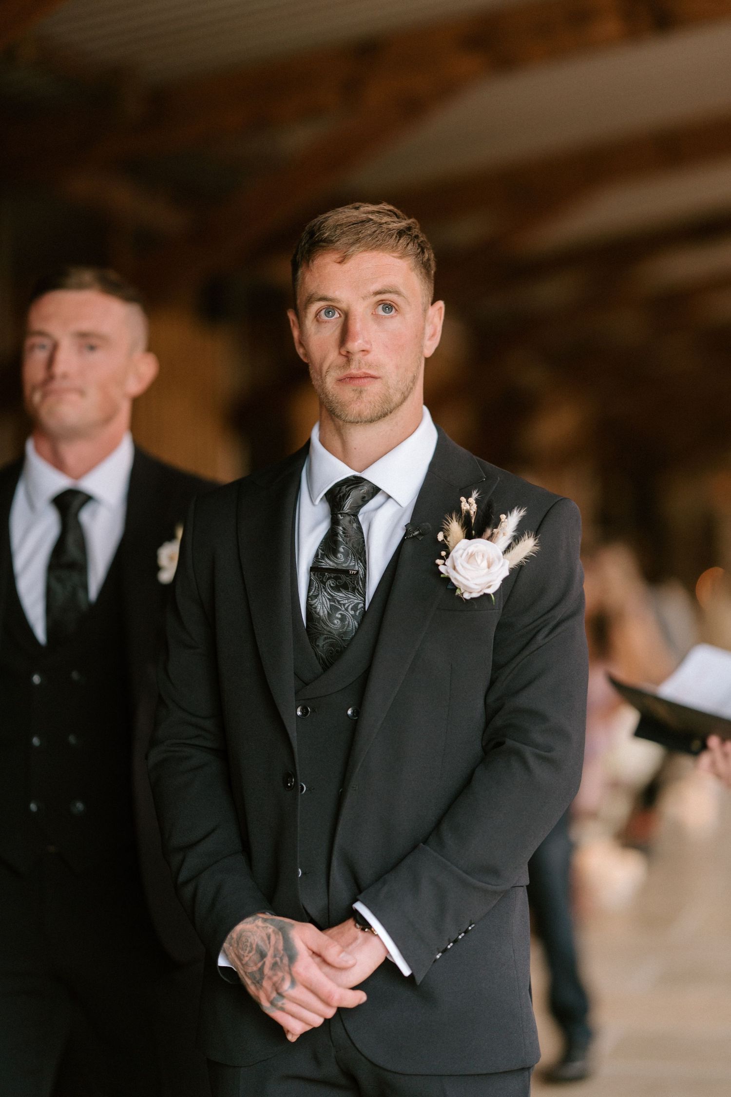 A groom shows emotional reactions during the wedding ceremony while wearing a classic black suit and white boutonniere.
