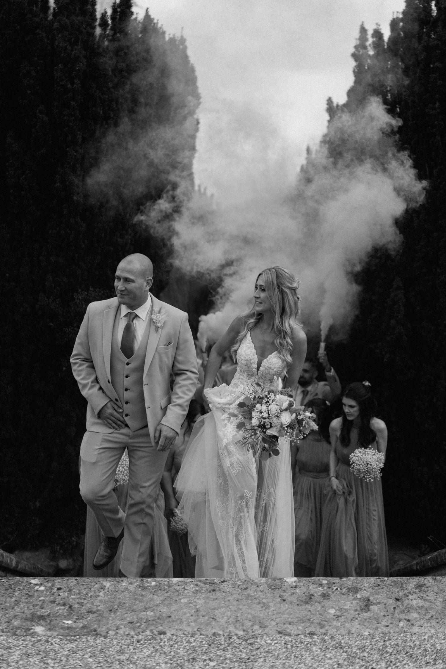A dramatic black and white wedding photo with smoke effects and a bridal party on a path in Warwickshire.
