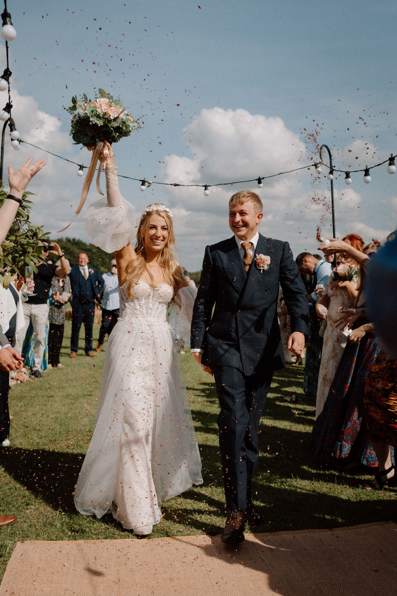 Joyful newlyweds walk through pathway of guests during outdoor wedding celebration.