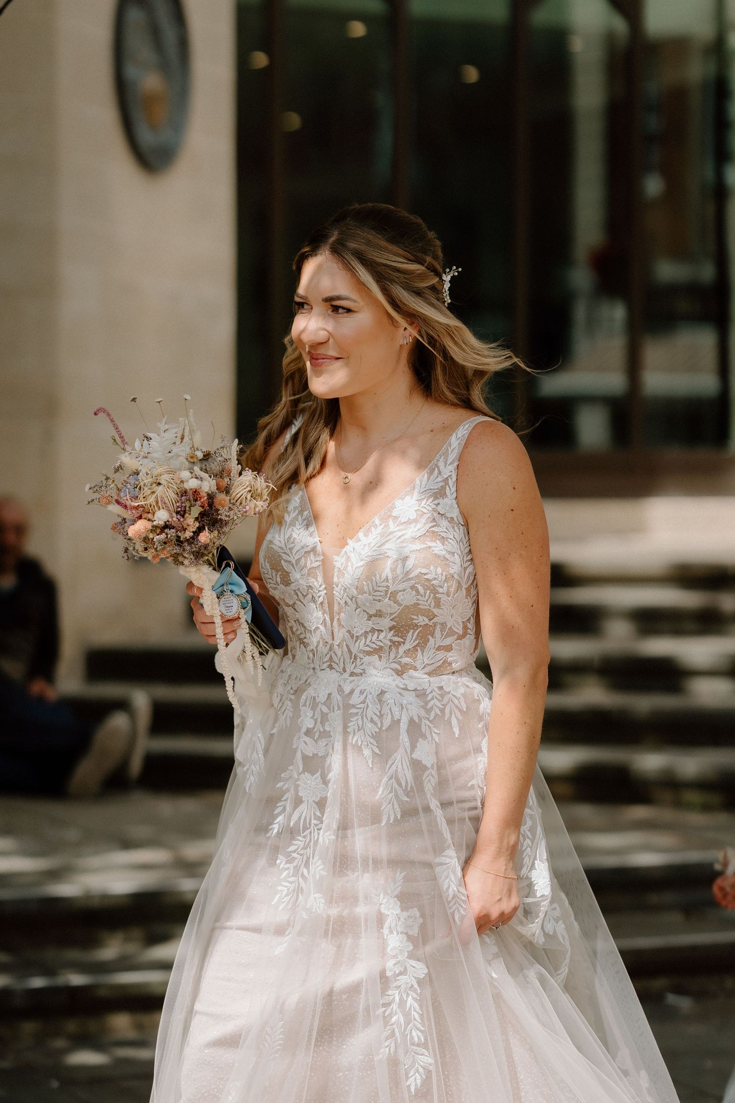 A bride in a detailed lace wedding gown holds a delicate dried flower bouquet outdoors in Northampton.