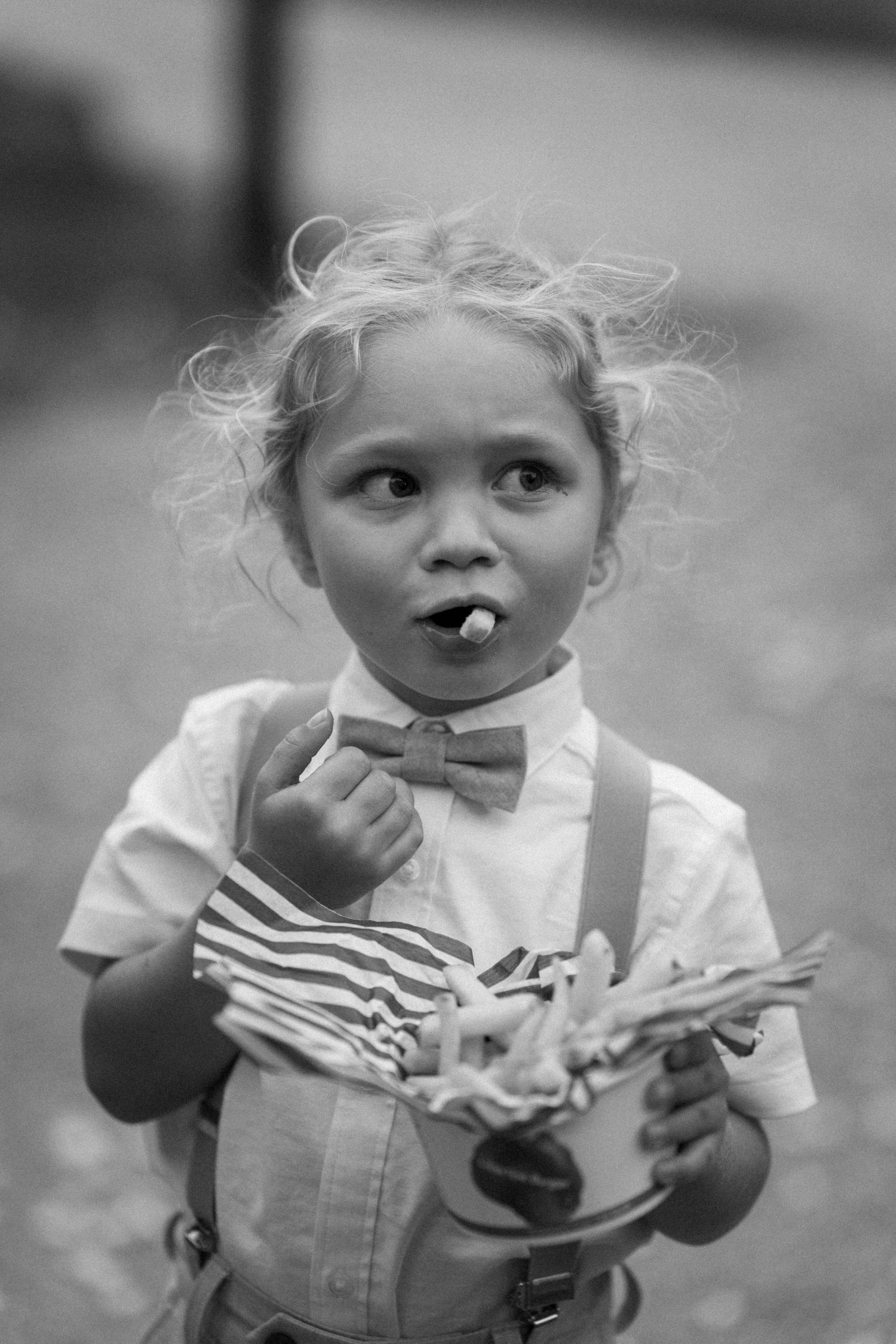 Young child in bow tie and suspenders eating snacks at formal event.
