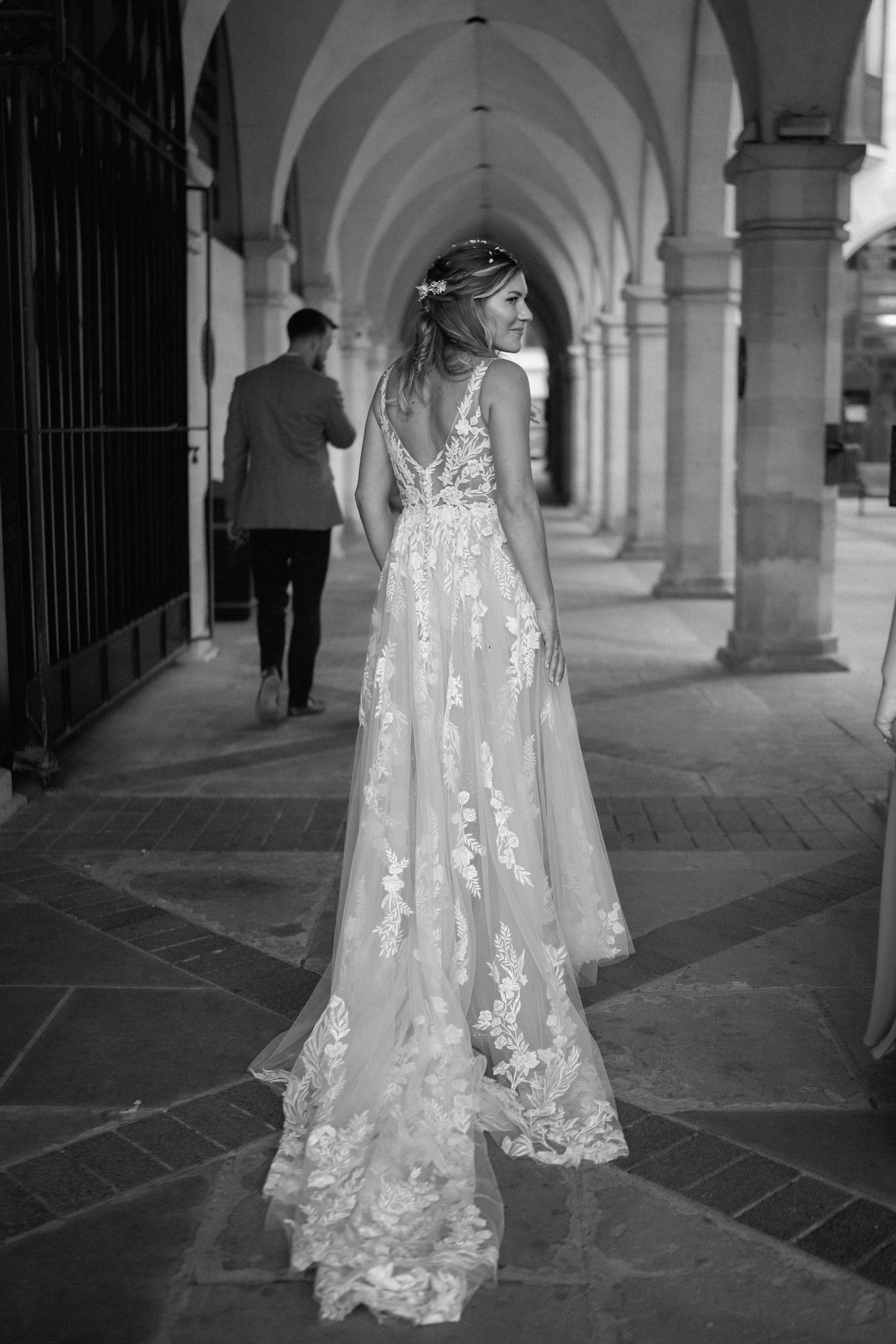A bride in a delicate lace wedding gown walks through an elegant arched corridor in black and white in Northampton.