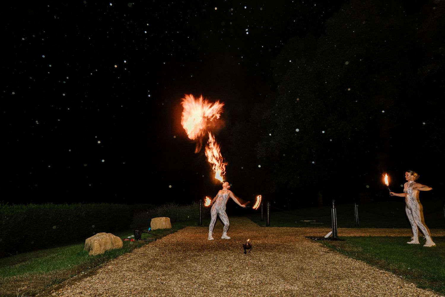 Fire performers twirl flaming batons against a starlit night sky.