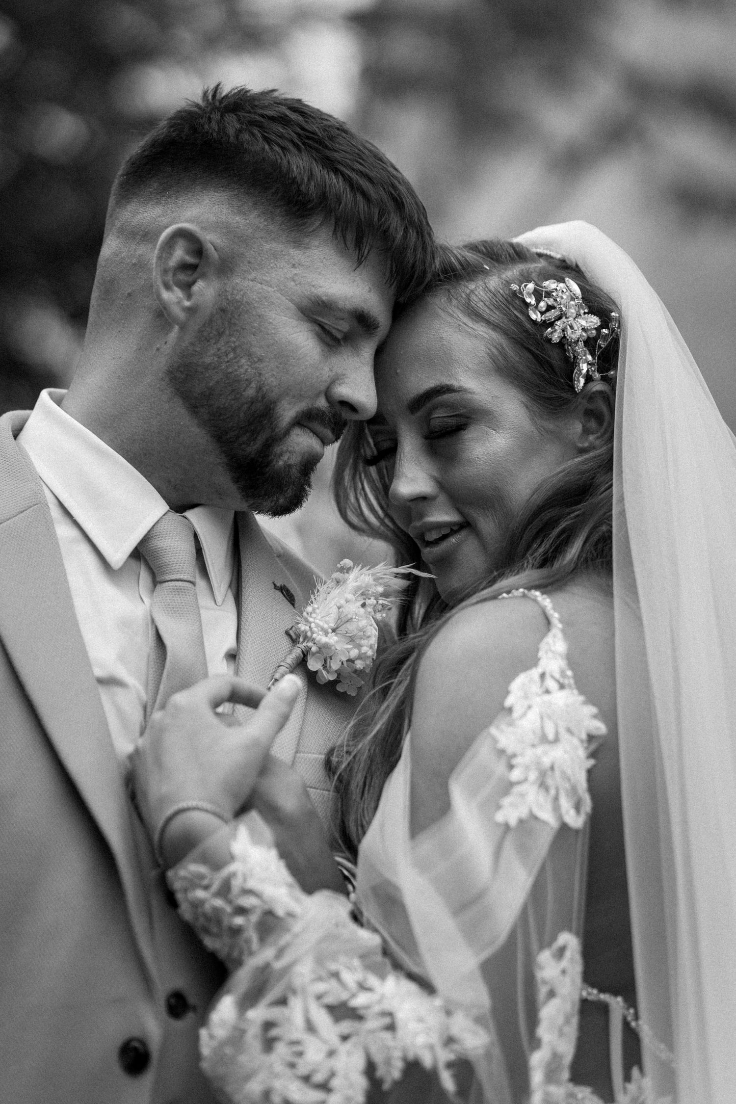 An intimate black and white portrait of a couple sharing a tender moment in wedding attire.