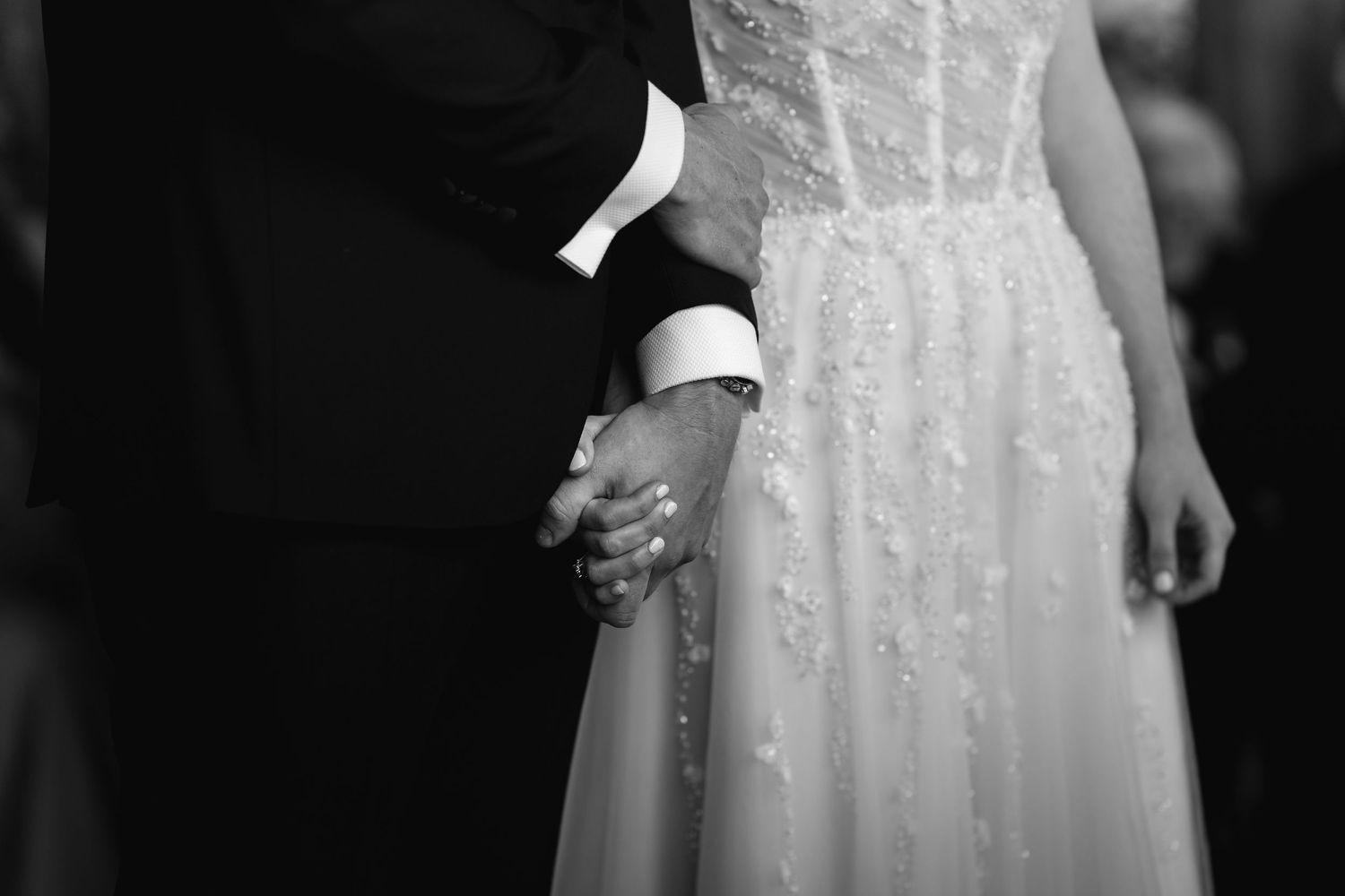 Black and white wedding photo of bride and groom holding hands, bride in lace gown.