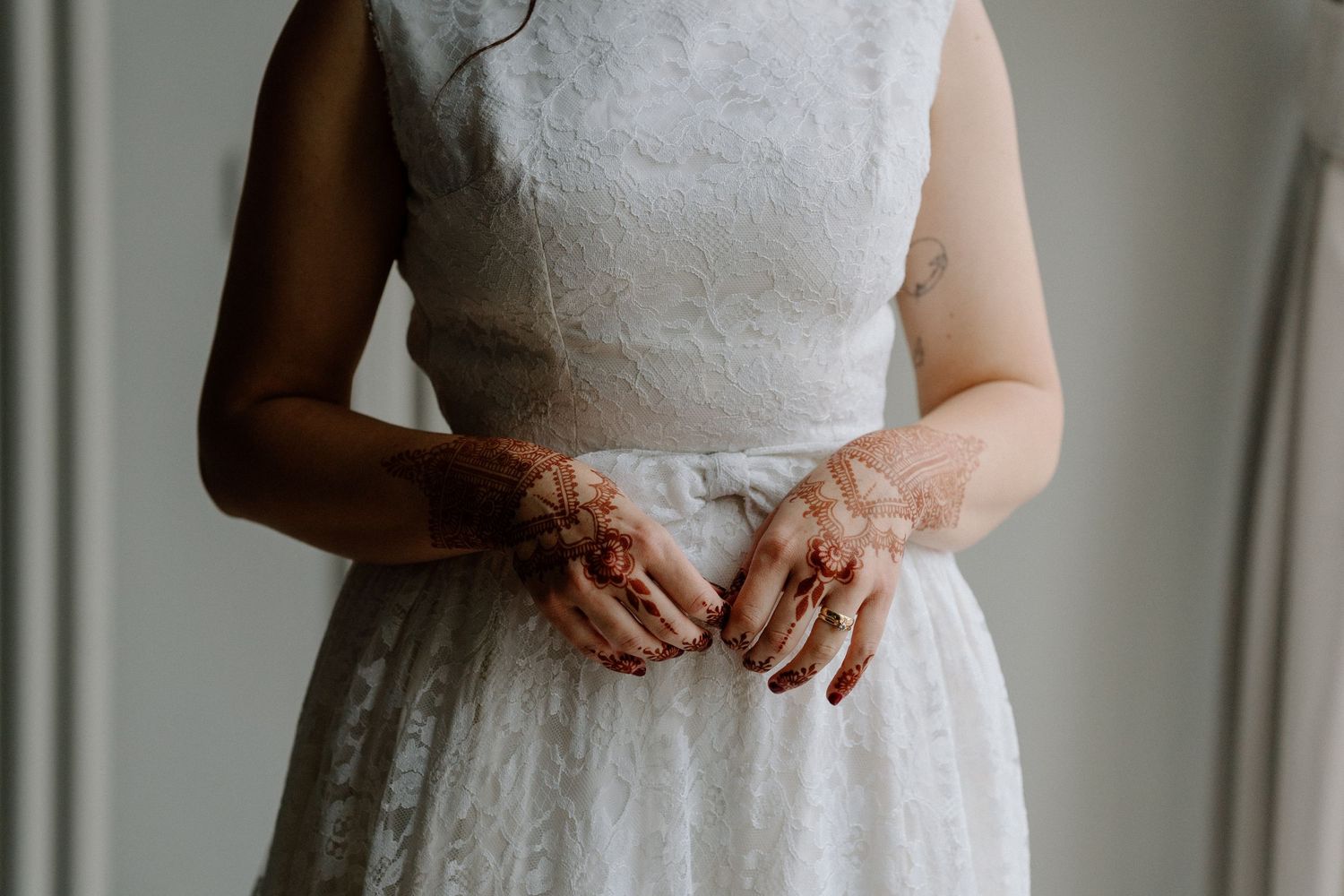 Close-up of a bride's midsection showing lace wedding dress details and clasped hands.