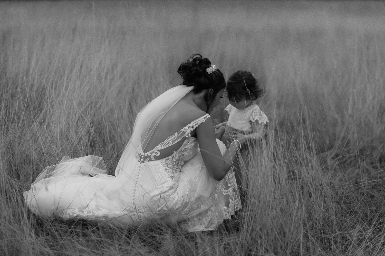 A tender moment captured in black and white as figures embrace in a field of tall grass.