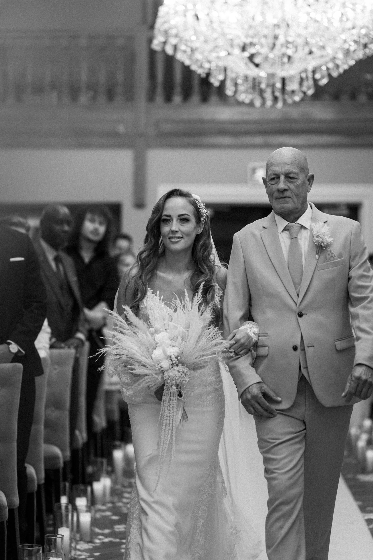 A wedding ceremony processional along a candle-lit aisle under an elegant crystal chandelier.