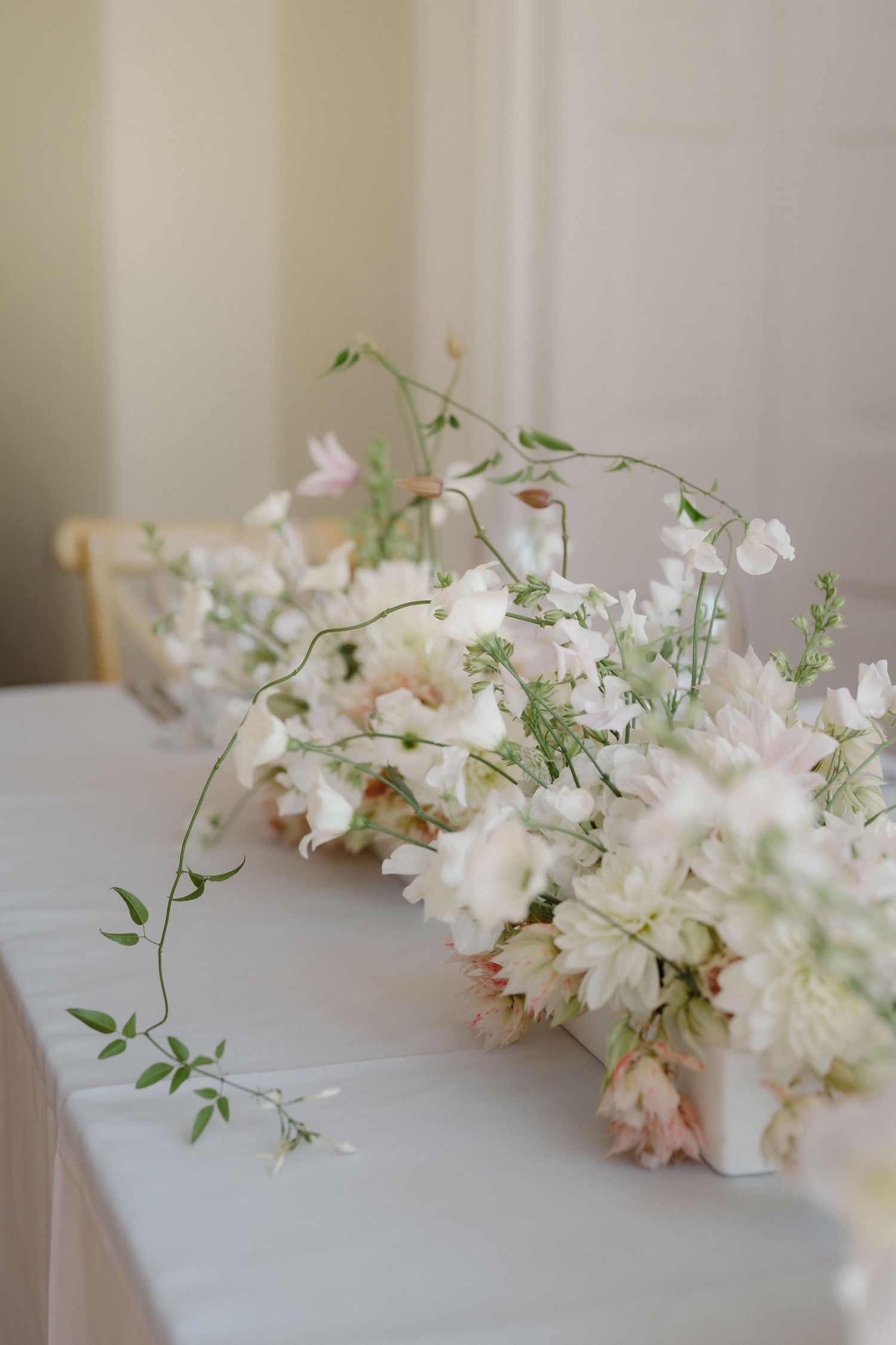 Delicate white and blush floral centerpiece arrangement on white tablecloth for wedding reception.