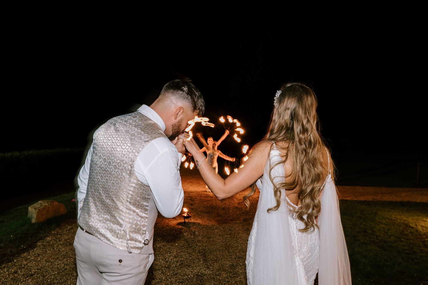 Couple dancing under starlit sky with sparklers creating romantic ambient lighting at outdoor wedding reception.