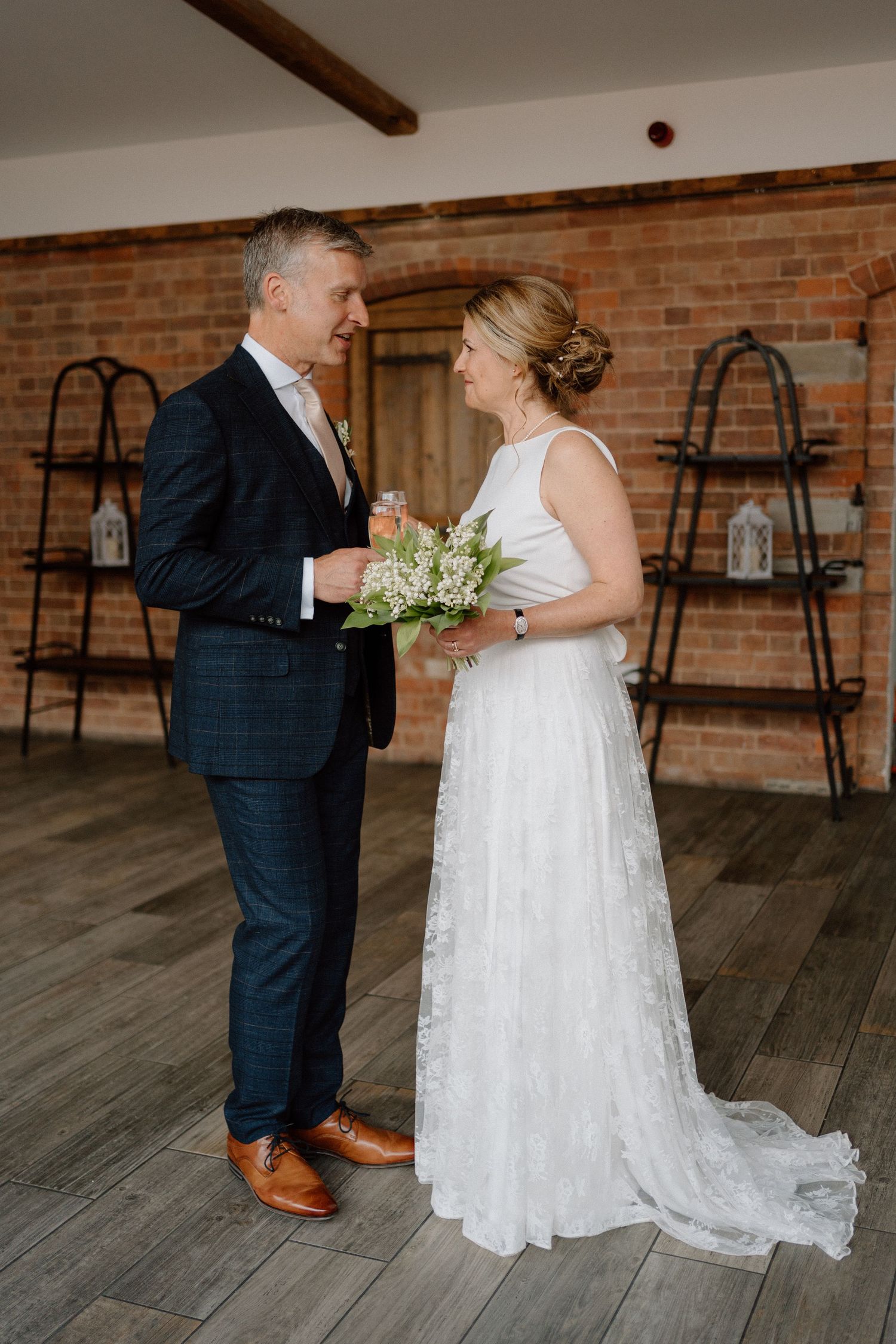A couple in wedding attire share a tender moment on rustic wooden floor with exposed brick walls and lanterns at Swallows Nest Barn.