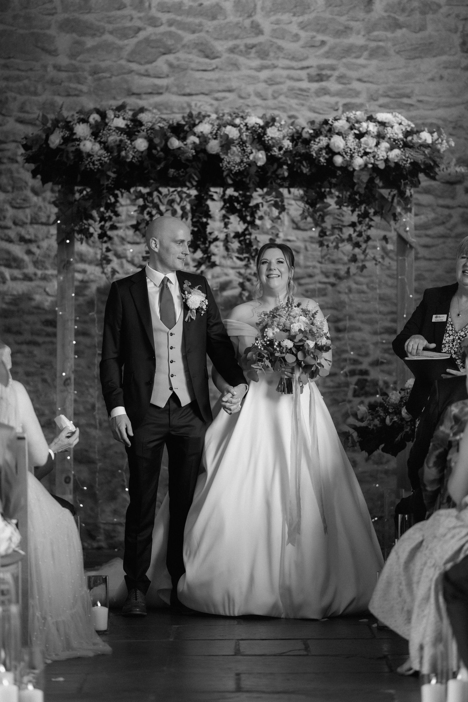 Wedding ceremony under floral arch with stone wall backdrop at Dodford Manor.