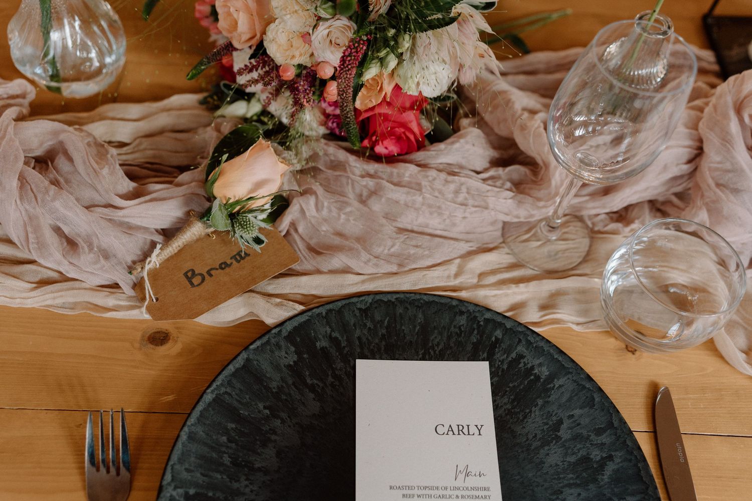 Elegant table setting with floral centerpiece, menu card, and gray charger plate on wooden surface at The Old Cow Shed.