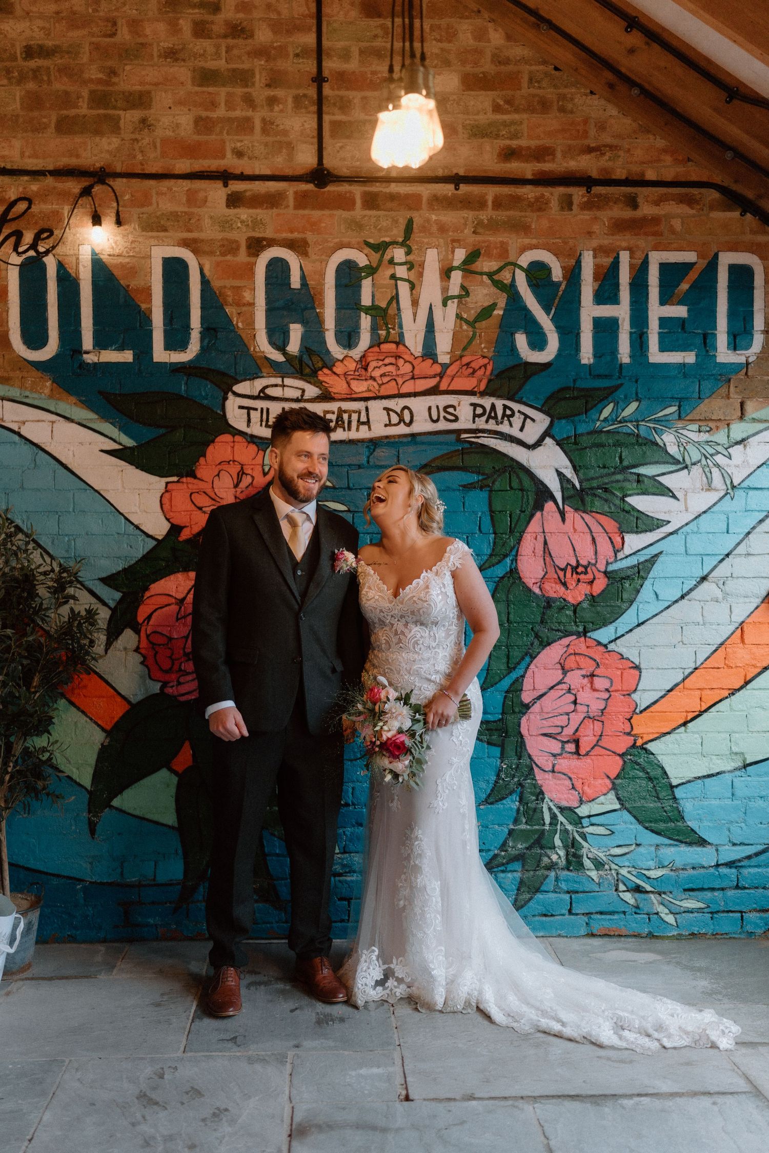 Wedding portrait against colorful mural wall with floral design and 'Old Cow Shed' text at The Old Cow Shed.