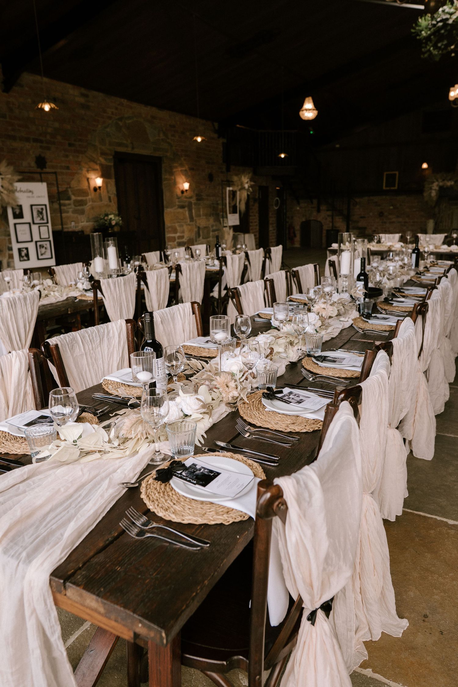 Elegant wedding reception table setting with white chair covers and rustic decor in stone-walled venue.