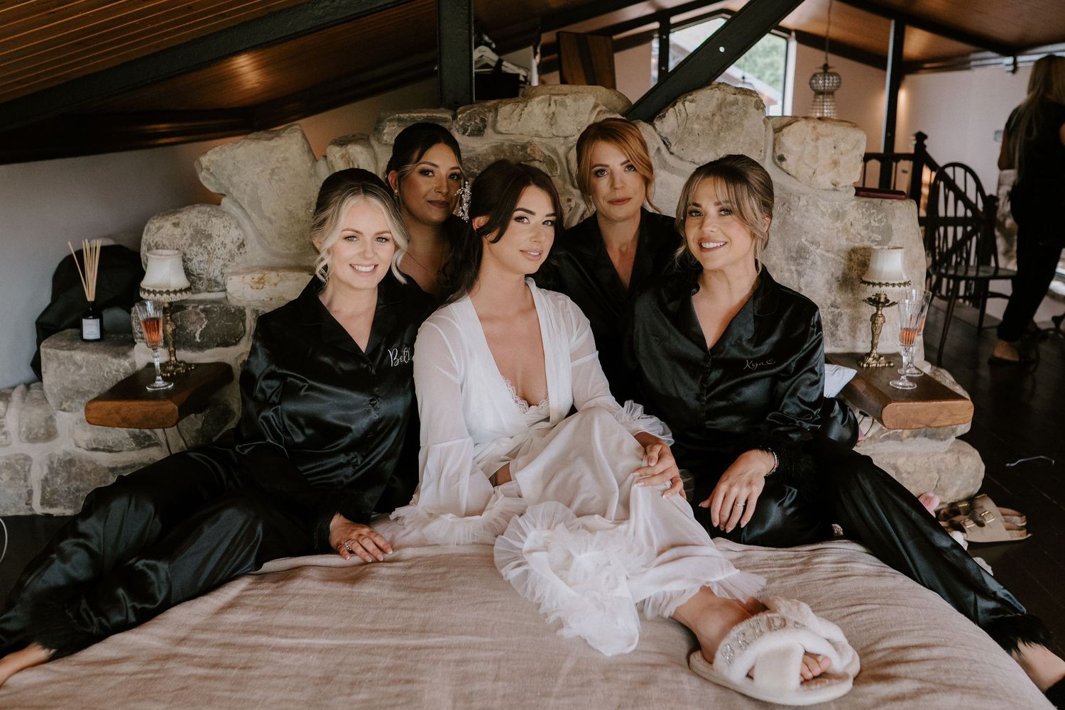 People wearing matching black and white silk robes sit together on a bed during a wedding preparation moment.