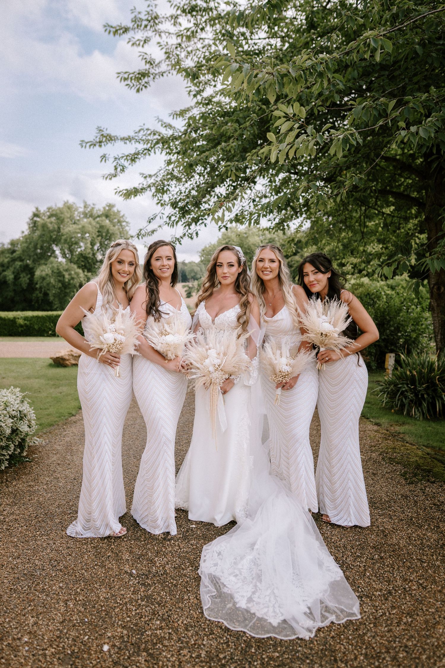 Wedding party in white dresses poses together on garden path.