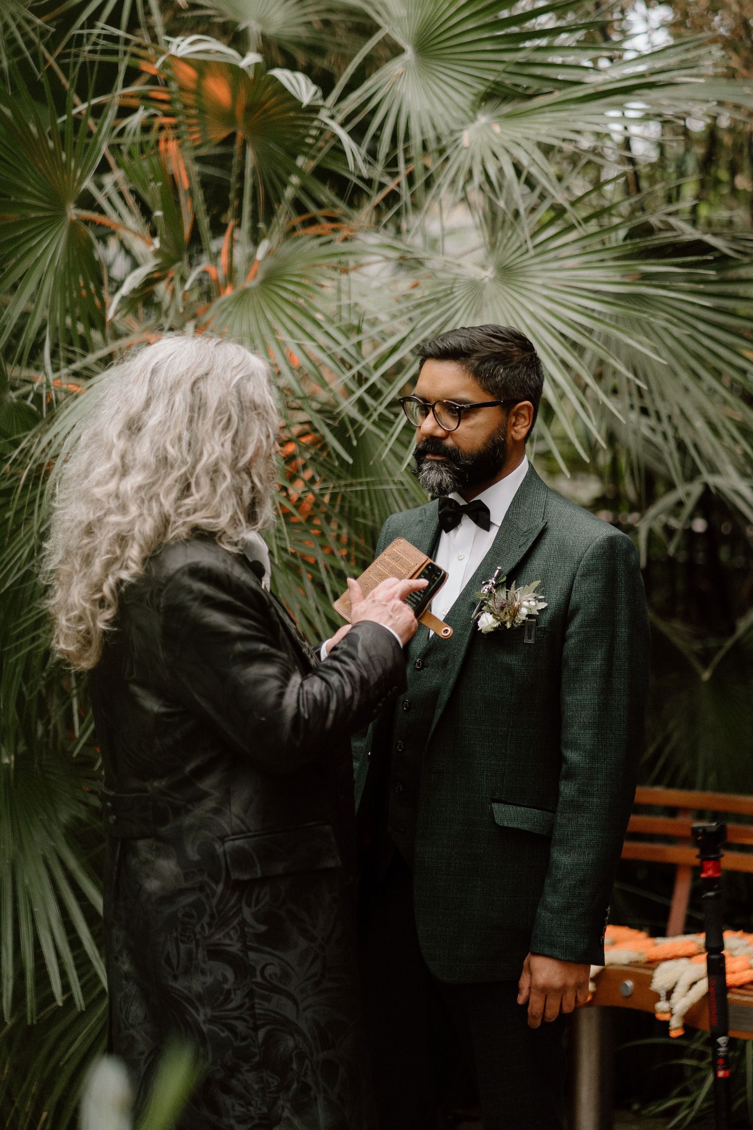 A pre-wedding moment with the groom getting his boutonniere pinned in front of tropical palm leaves at The Glasshouse in Leamington Spa.