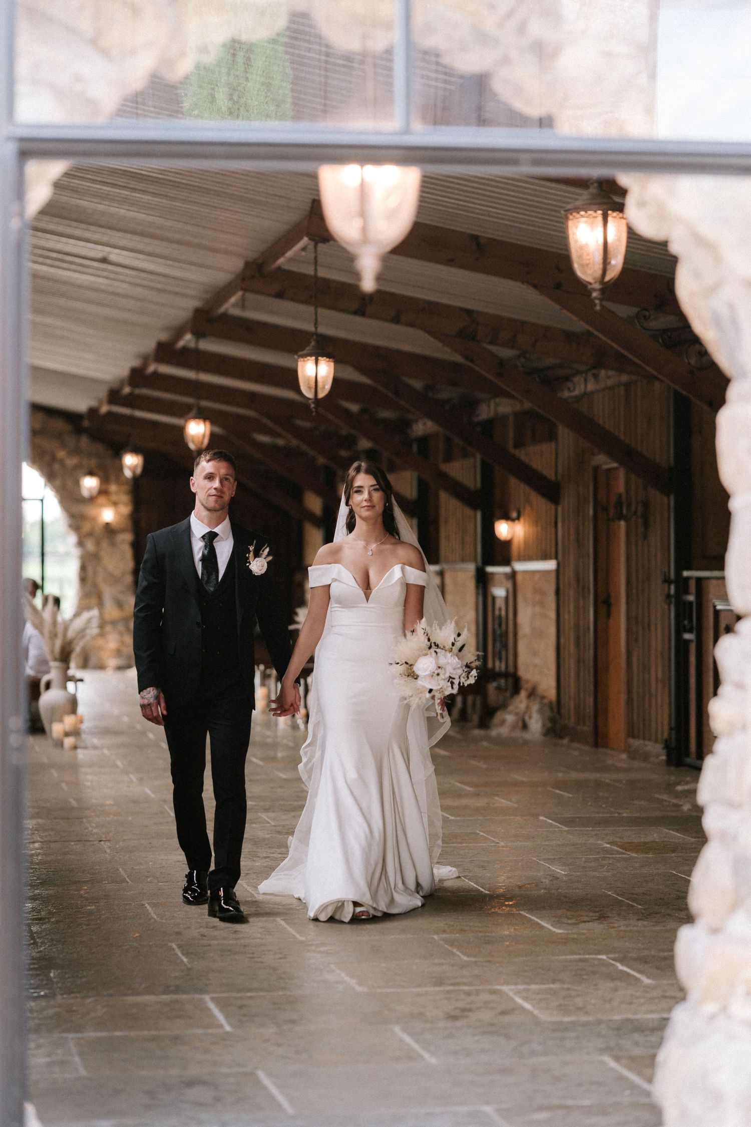 A couple walks together under an ornate covered walkway decorated with vintage lanterns on their wedding day.