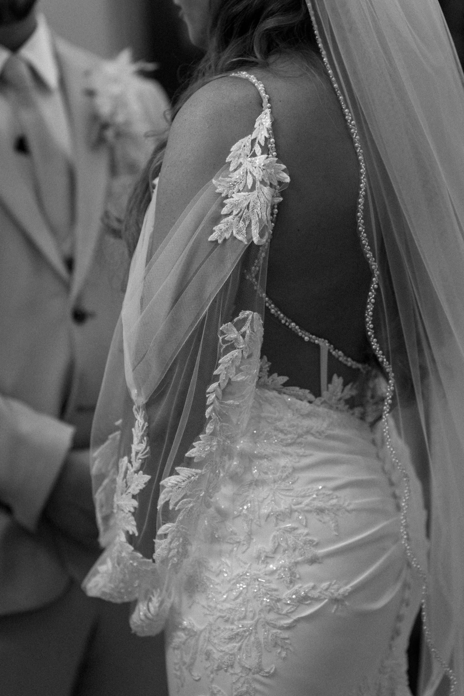 Close-up detail of delicate lace appliques and beading on a white wedding dress and veil. Wedding photography at Rushton Hall.