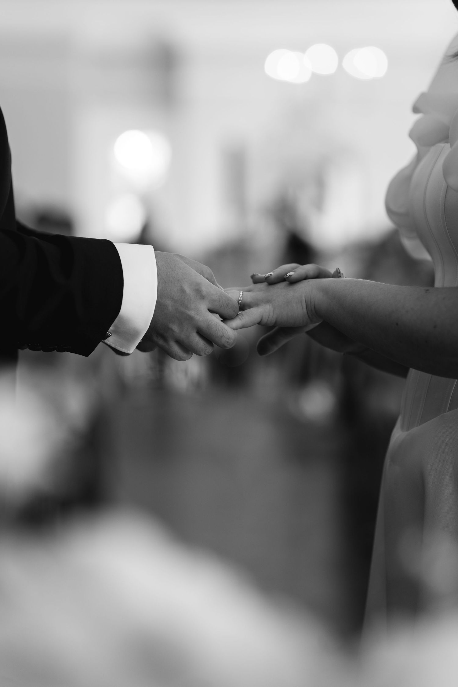 Black and white photo of bride and groom holding hands during wedding ceremony in church.