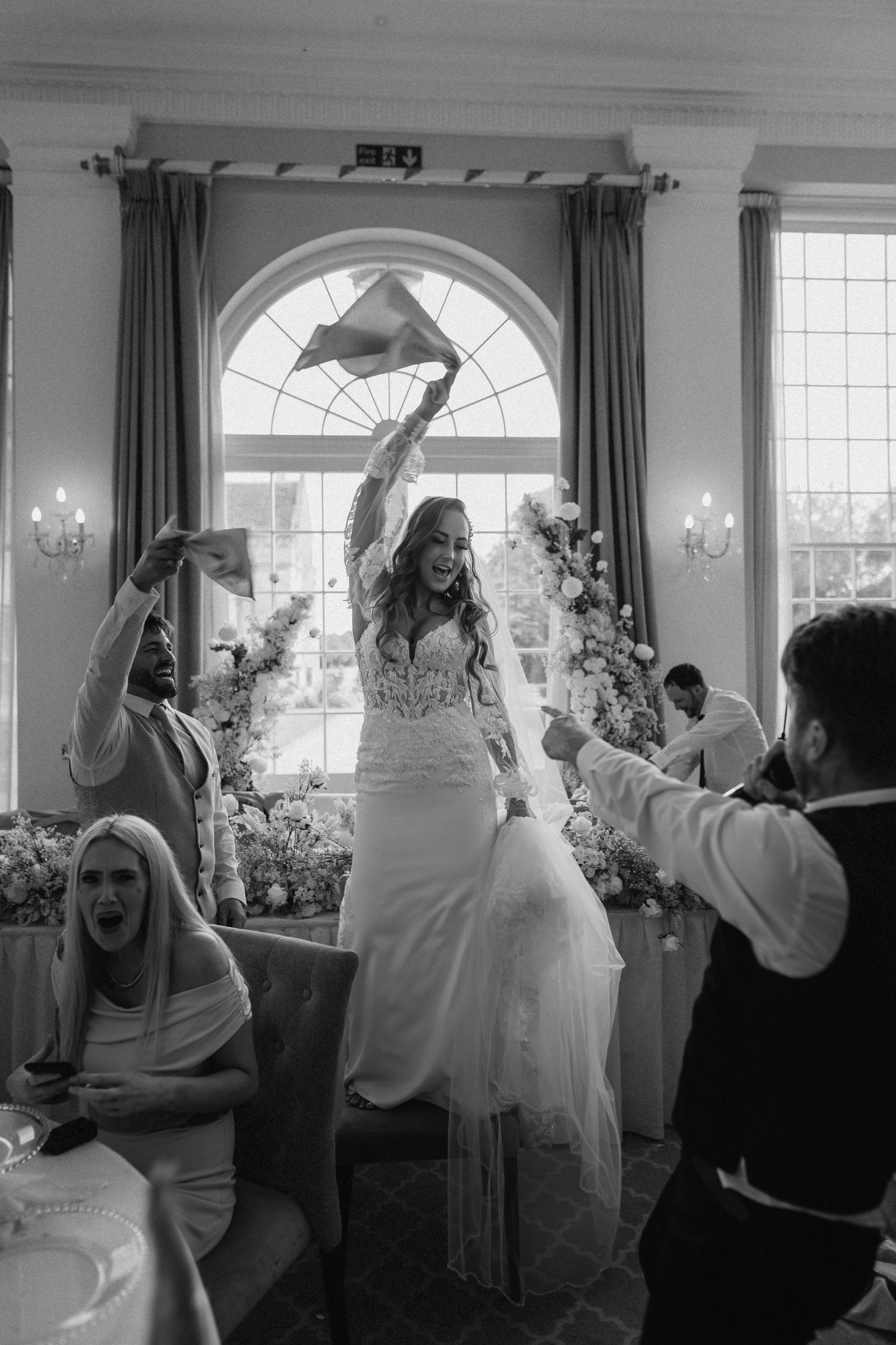 A celebration in an elegant reception hall with a stunning arched window and flowing curtains.
