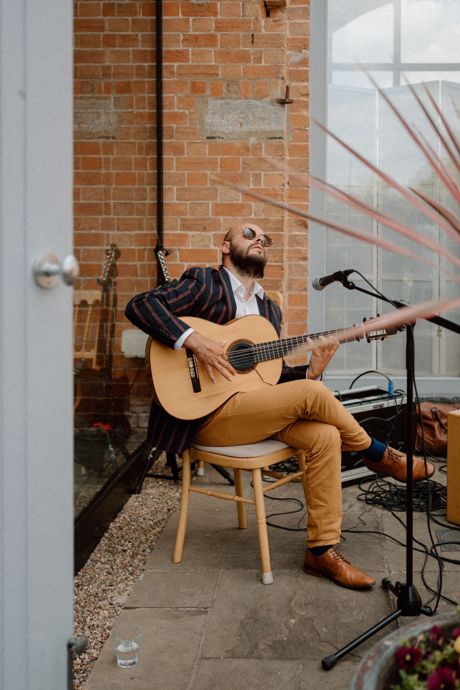 A musician plays acoustic guitar while seated on a wooden stool against an exposed brick wall at Swallows Nest Barn.