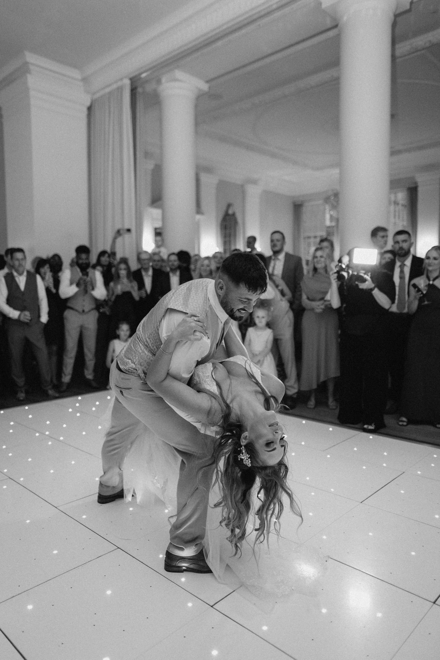 A dramatic black and white photo of a dance performance on an illuminated floor in an elegant ballroom.