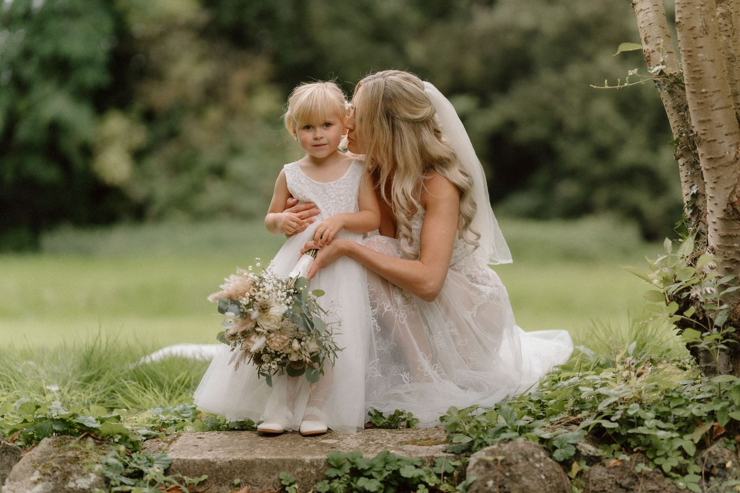 Sweet moment between bride and flower girl in matching white dresses outdoors in Warwickshire.