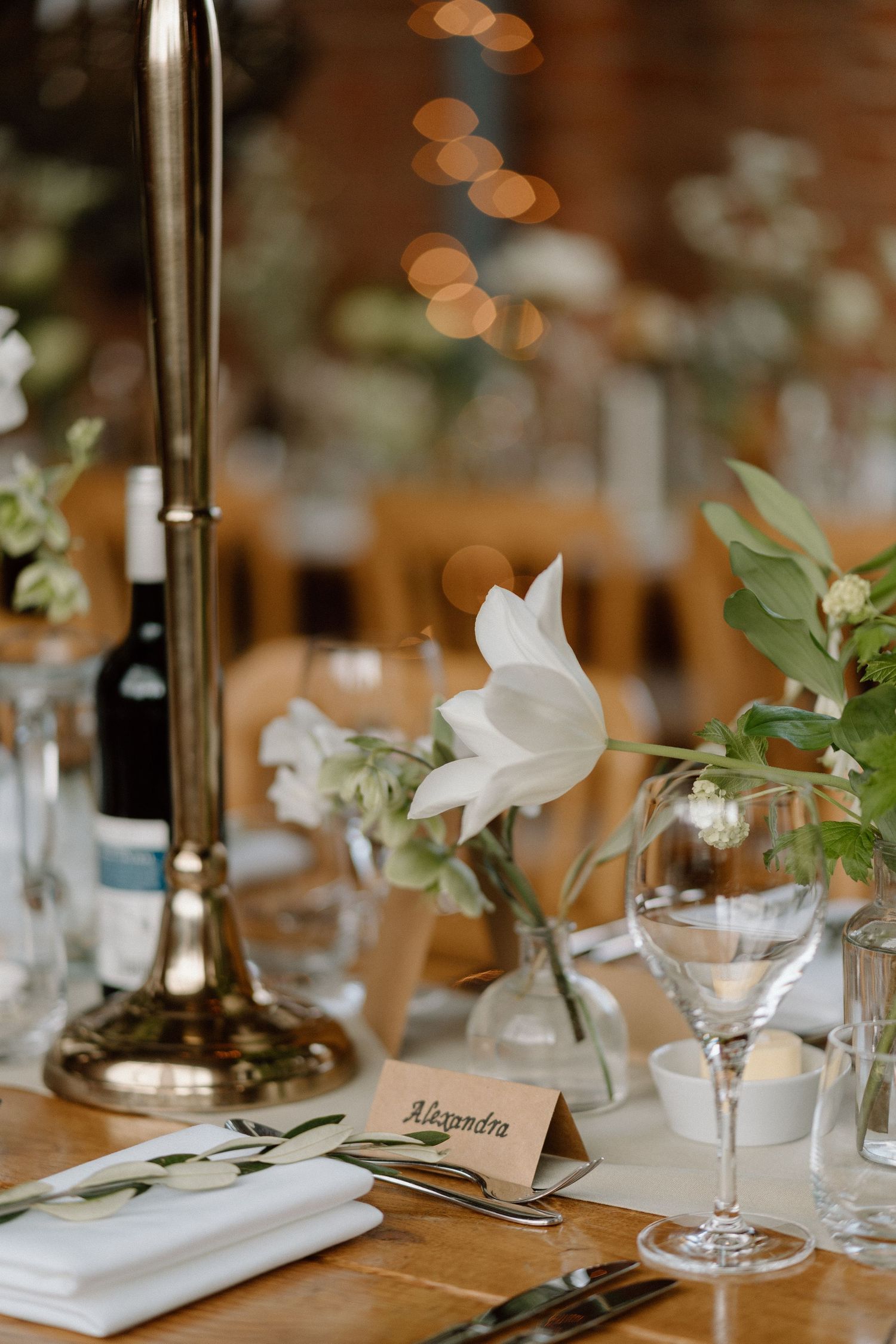 Elegant table setting with white magnolia flower, wine glass, and place card on rustic wooden surface at Swallows Nest Barn.