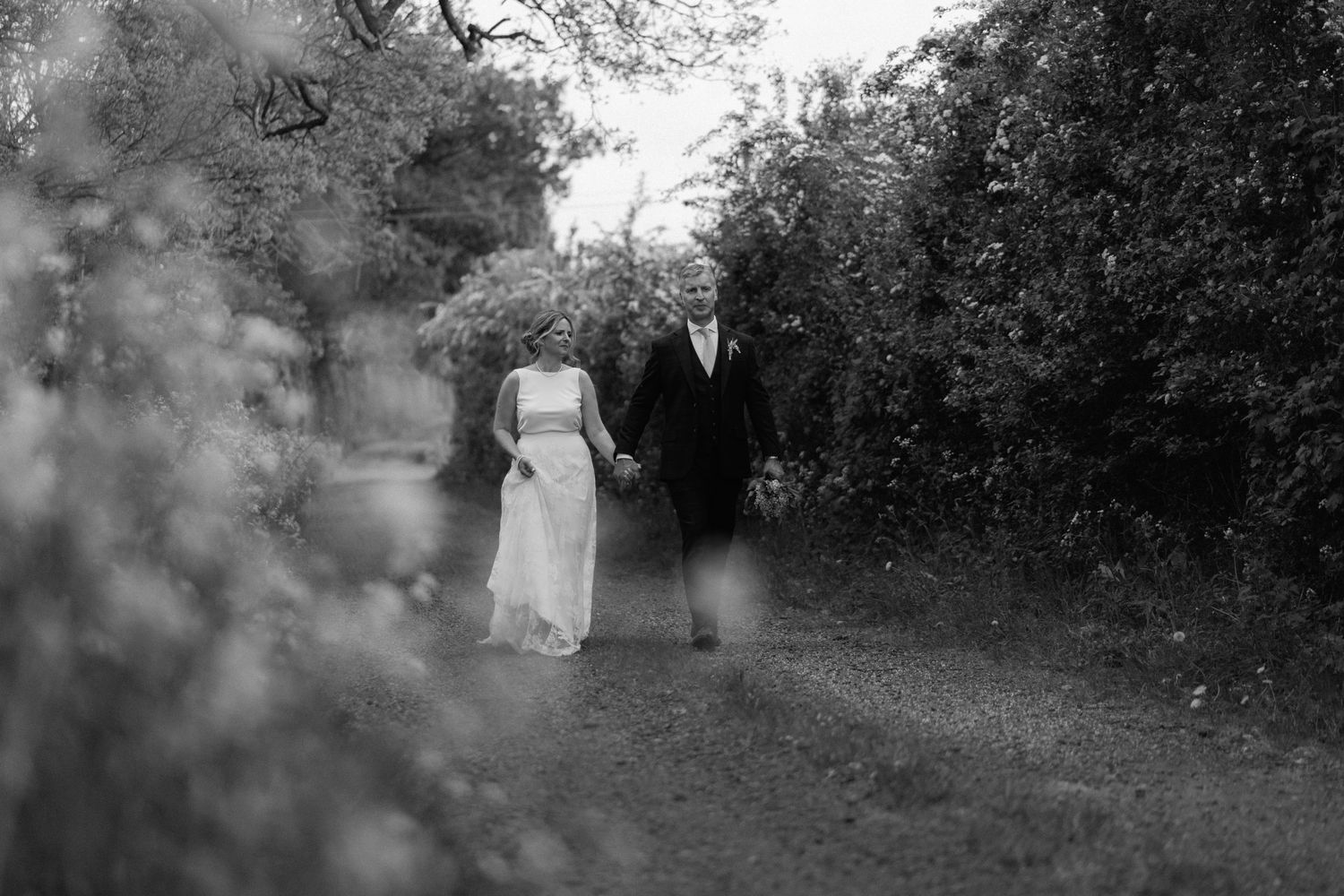 A black and white romantic vintage wedding photo of a couple walking together on a garden path at Swallows Nest Barn.