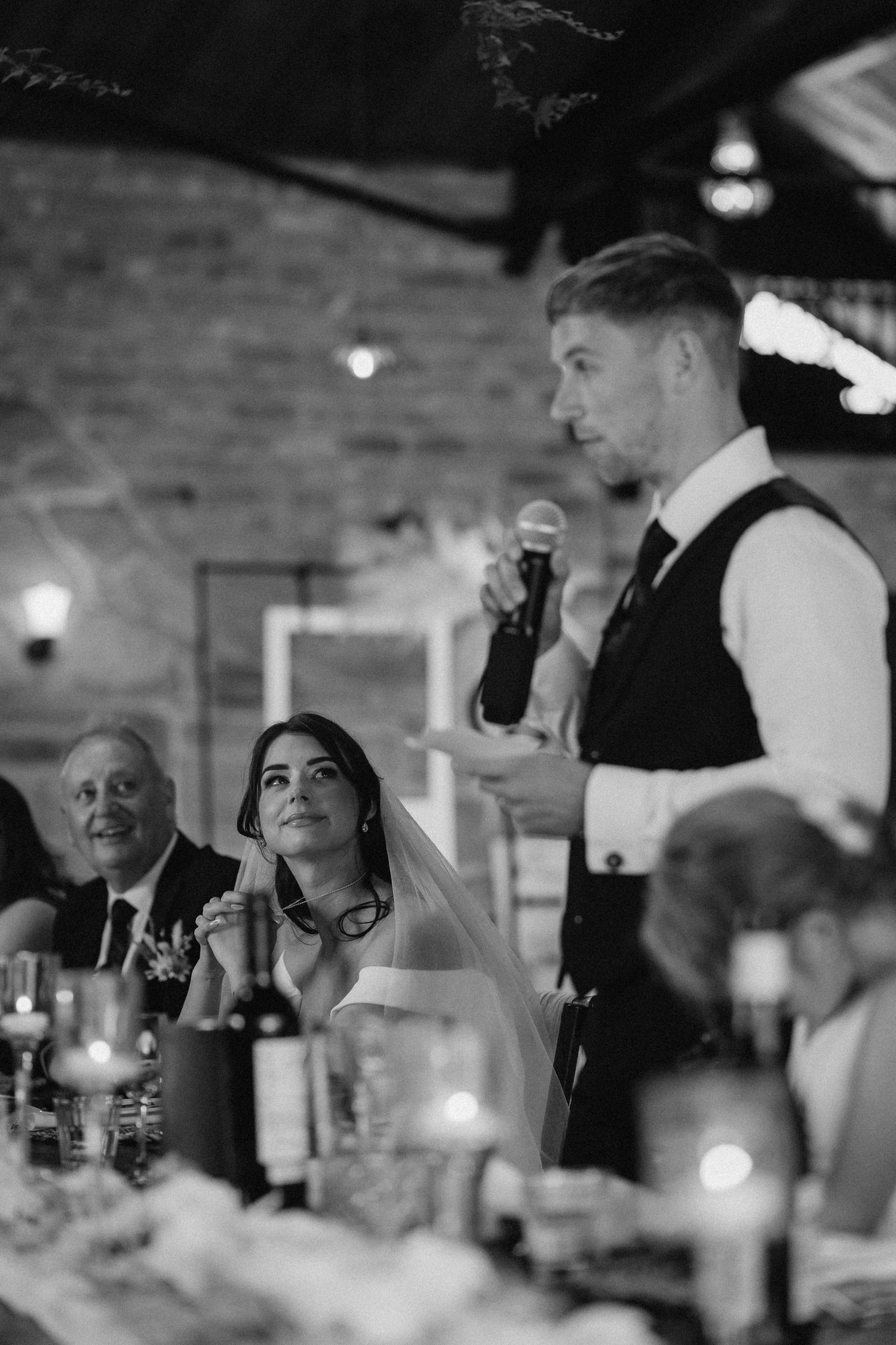 Wedding reception guests engaged in conversation at a rustic venue with brick walls.
