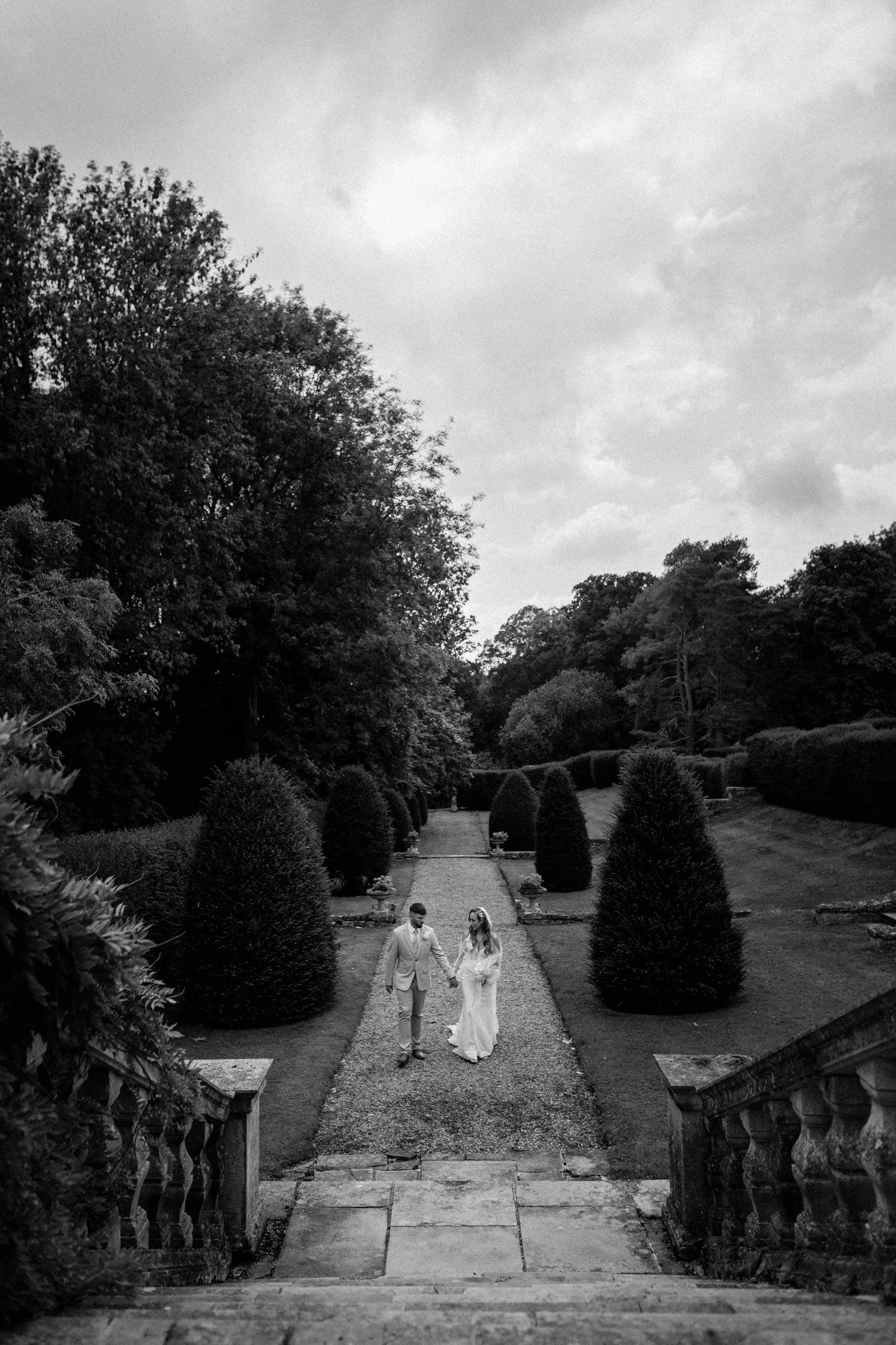 Black and white photo of couple walking down grand stone staircase in formal garden.