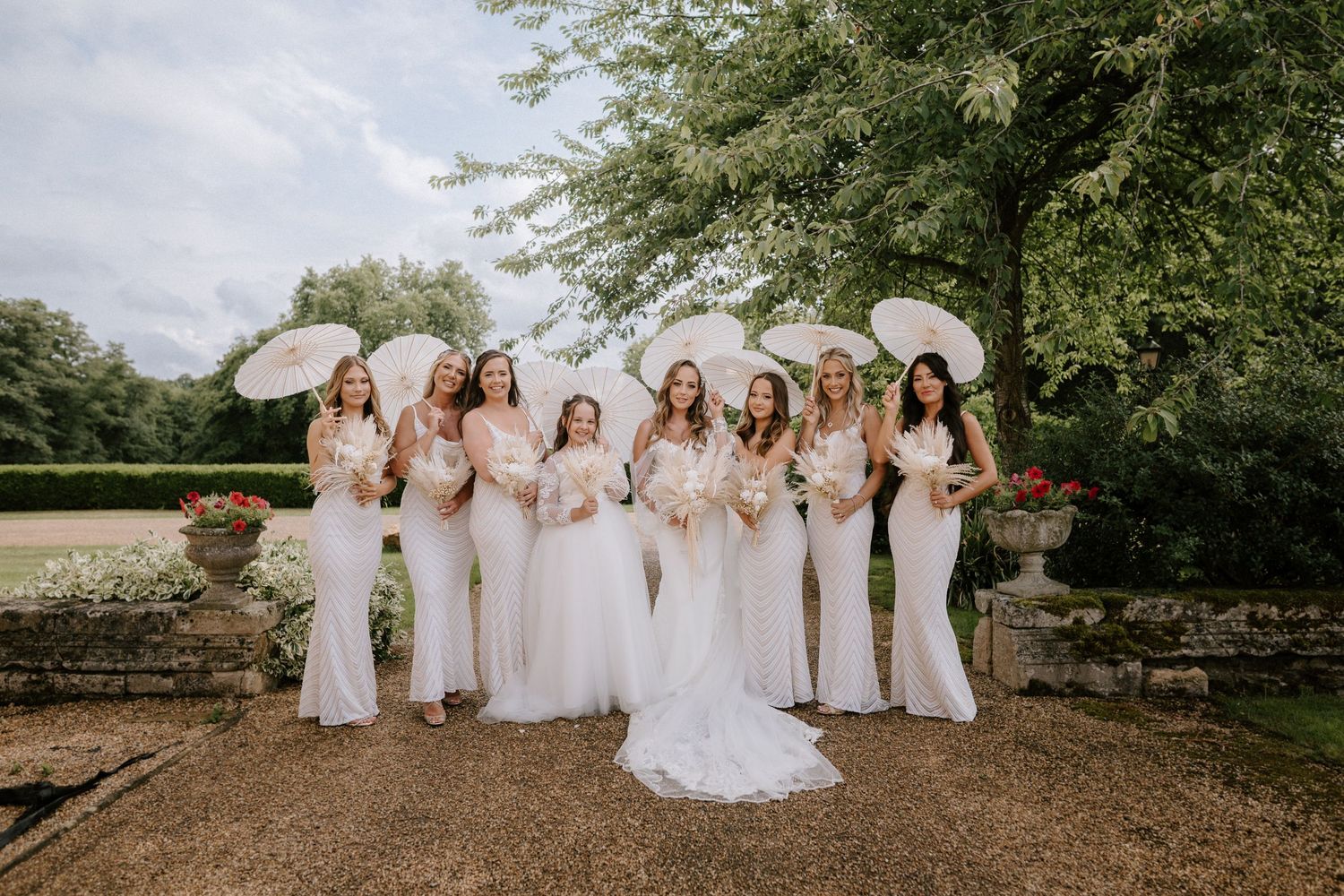 Group photo of bridesmaids in white dresses holding parasols at a Wedding. Wedding photography at Rushton Hall. Northamptonshire Wedding