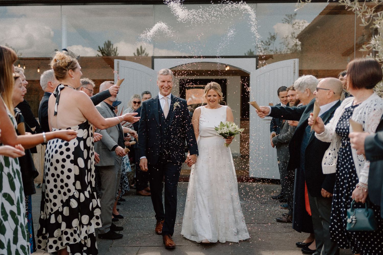 Wedding guests throw confetti over a smiling couple leaving a venue in a joyful outdoor celebration at Swallows Nest Barn.
