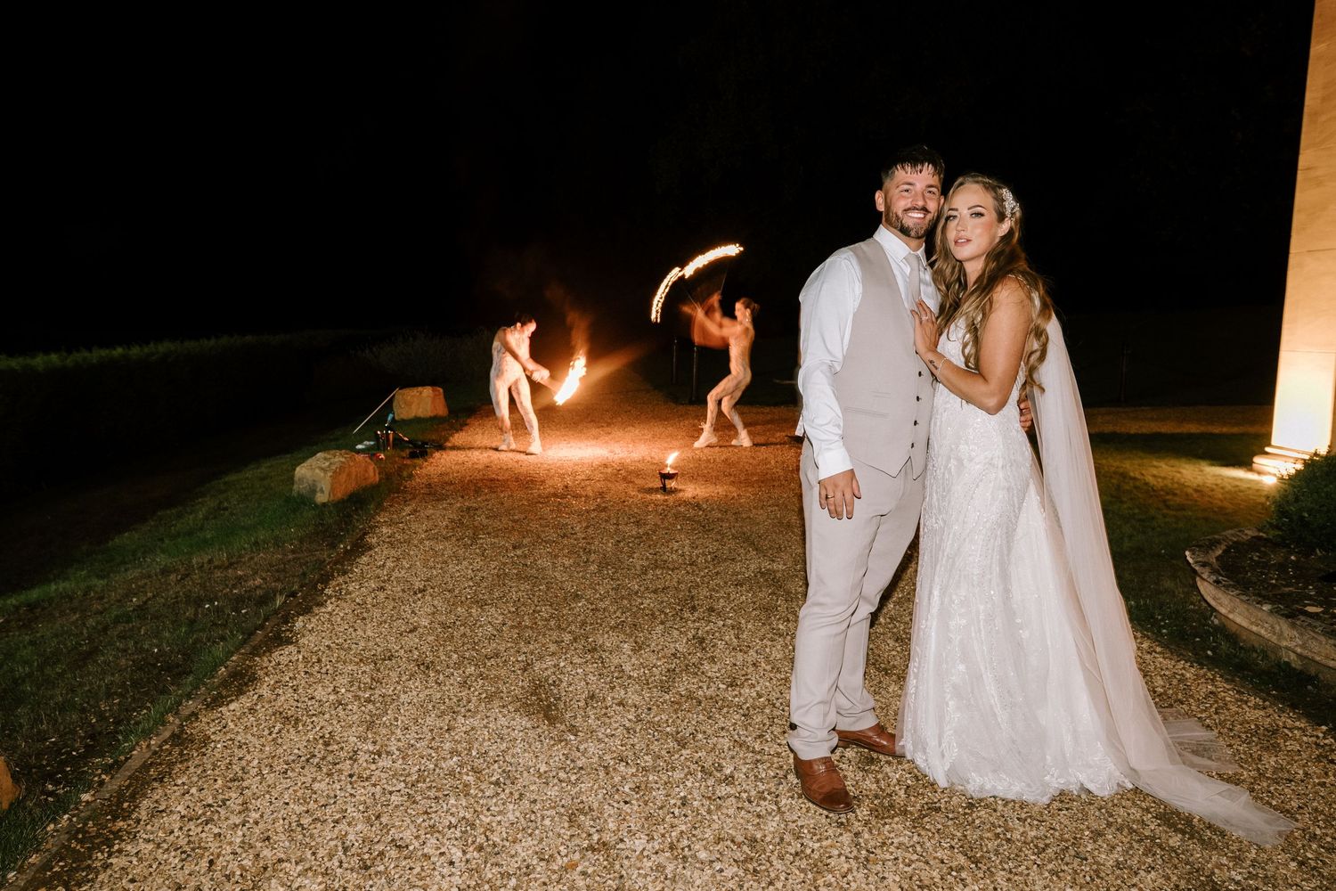 Wedding couple posing with fire performers creating light trails in background.