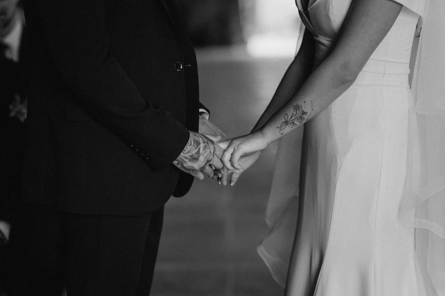 Black and white close-up photo of a couple holding hands during their wedding ceremony.
