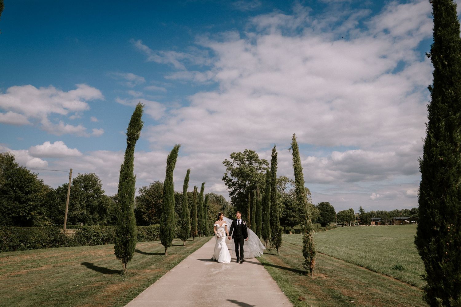 Scenic garden path lined with tall cypress trees and blue sky on a wedding day.