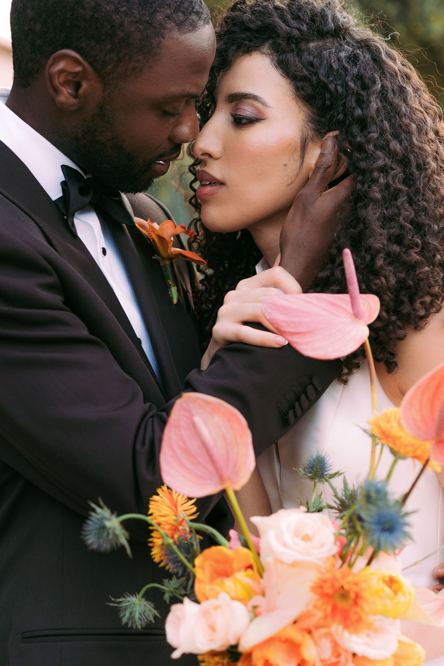 Romantic couple embracing with coral and orange floral bouquet details.