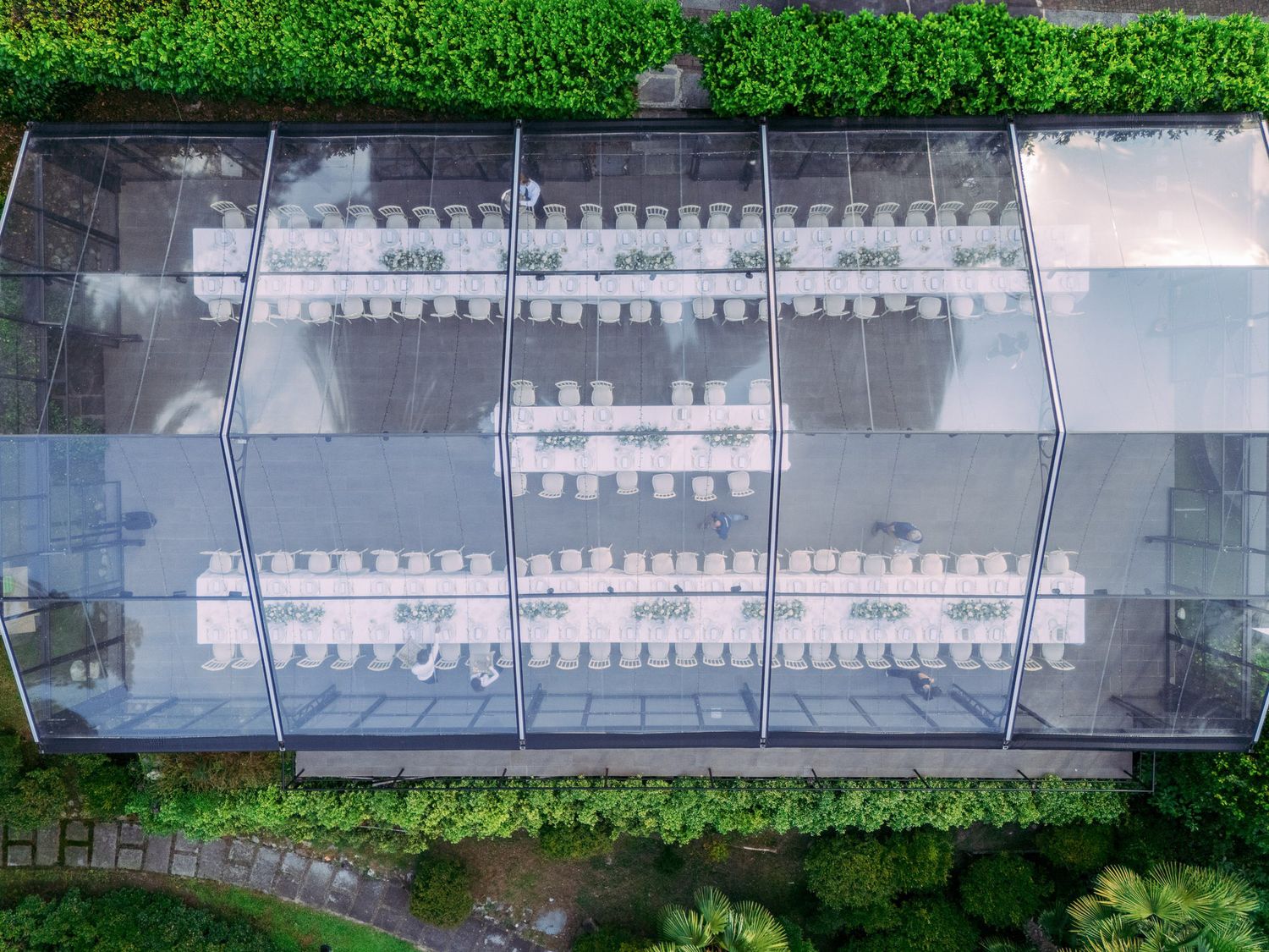 Aerial view of a long greenhouse structure with white panels and green vegetation visible on the sides.