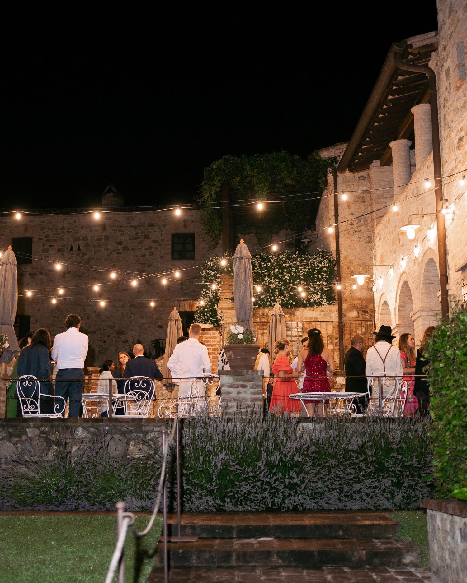 String lights illuminate an outdoor stone patio dining area at night with tables set for evening service.