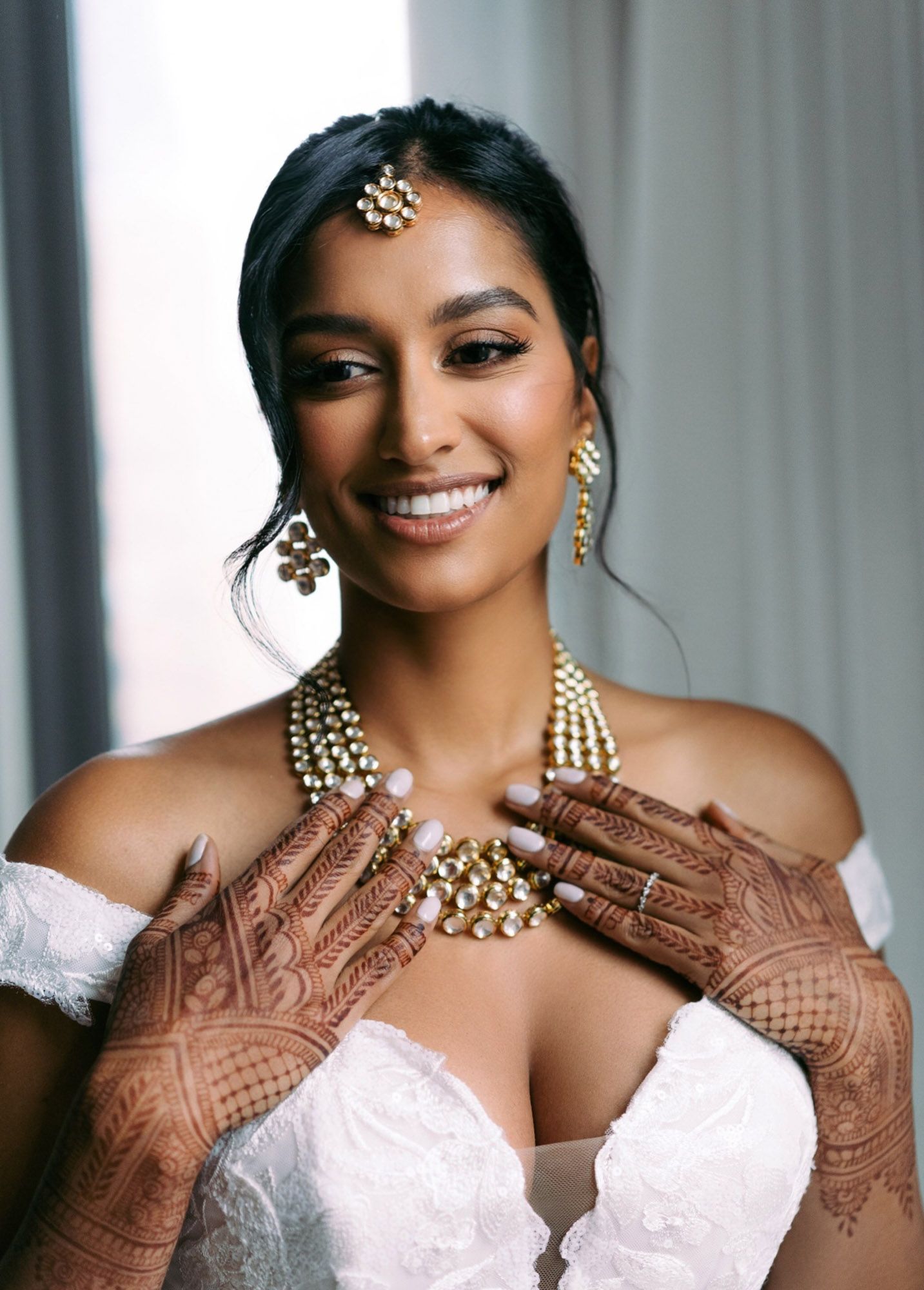 A person wearing a brown embroidered dress and traditional Indian bridal jewelry poses in a portrait series.