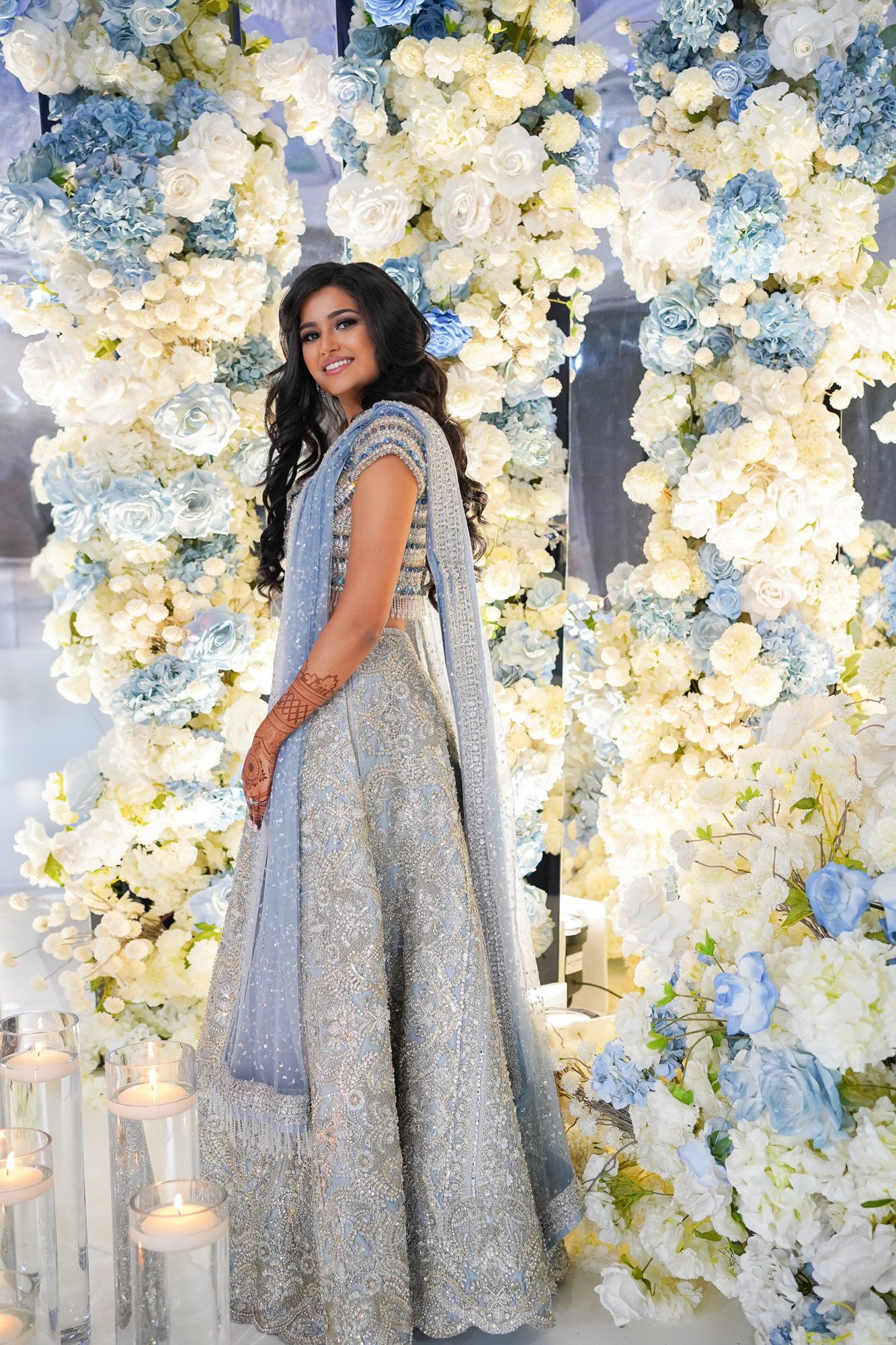 Elegant silver sequined gown photographed against a backdrop of white and blue floral arrangements.