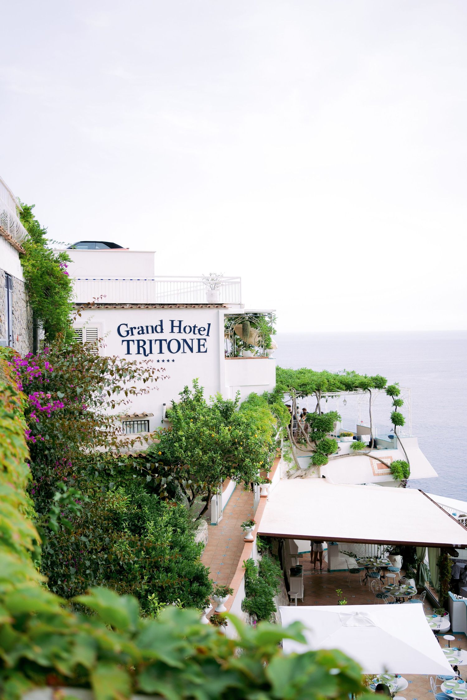 Exterior view of Grand Hotel Tritone perched on a scenic coastal hillside with lush greenery and white umbrellas.